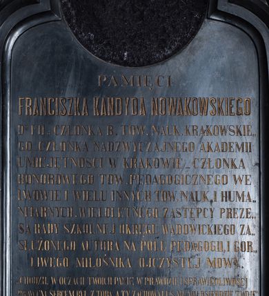 Zdjęcie nr 2: Epitafium w formie stojącego prostokąta,  ujęte szerokim obramieniem, z głęboką płyciną z motywem oślego łuku z wpisanym w niego maswerkiem oraz z maswerkami w nadłuczach. Nad górną krawędzią ujęty dwiema ulistnionymi wolutkami krzyżyk łaciński o fazowanych krawędziach. W łuku okrągła płycina z polem na portret, poniżej inskrypcja „PAMIĘCI / FRANCISZKA KANDYDA NOWAKOWSKIEGO / D(OKTO)RA FIL(OZOFII) CZŁONKA B(IERNEGO) TOW(ARZYSTWA) NAUK(OWEGO) KRAKOWSKIE/GO CZŁONKA NADZWYCZAJNEGO AKADEMII / UMIEJĘTNOŚCI W KRAKOWIE_CZŁONKA / HONOROWEGO TOW(ARZYSTWA) PEDAGOGICZNEGO WE / LWOWIE I WIELU INNYCH TOW(ARZYSTW) NAUK(OWYCH) I HUMA/NITARNYCH. WIELOLETNEGO ZASTĘPCY PREZE/SA RADY SZKOLNEJ OKRĘGU WADOWICKIEGO ZA/SŁUŻONEGO AUTORA NA POLU PEDAGOGII, I GOR/LIWEGO MIŁOŚNIKA OJCZYSTEJ MOWY. / „CHODZIŁ W OCZACH TWOICH PANIE W PRAWDZIE I SPRAWIEDLIWOŚCI / PRAWEM SERCEM BYŁ Z TOBĄ, A TY ZACHOWAŁEŚ MU MIŁOSIERDZIE TWOJE". / Z KS(IĘGI) III KRÓL(EWSKIEJ) ROZ(DZIAŁ) 3. / *3 X 1813 W POZNANIU † 19 XI 1881 W SUCHY. / NAJZACNIEJSZEMU MĘŻOWI ŻONA / PROSI POBOŻNYCH  O MODLITWĘ.”

