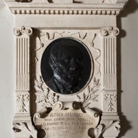 Zdjęcie nr 1: Epitafium w formie aediculi, flankowane przez kanelowane pilastry z jońskimi kapitelami. Powyżej pełne belkowanie z wysokim fryzem, gzymsem ozdobionym kostkowaniem i przerwanym przyczółkiem w kształcie luku nadwieszonego, z krzyżem łacińskim pośrodku. W polu medalion z płaskorzeźbionym portretem zmarłego, otoczony tasiemkami i liśćmi laurowymi oraz dębowymi. Poniżej, w kartuszu, inskrypcja: &quot;ALFRED OBALIŃSKI / PROF(ESOR) CHIRUR(GII) UNIW(ERSYTETU) JAGIELL(OŃSKIEGO) / * 15. GRUDNIA 1843. W BRZEŻANACH / † 18 LIPCA 1898 W KRAKOWIE. / Ku wiecznej pamięci / kamień ten położyli koledzy / Tow(arzystwa) Lek(arskiego) Krakowskiego / i Prof(esorowie) Uniwersytetu&quot;.