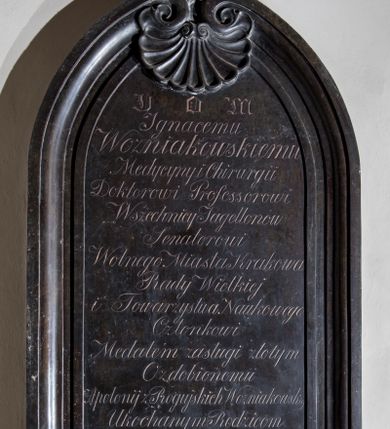 Zdjęcie nr 1: Epitafium w kształcie stojącego prostokąta, zamkniętego dwiema, półkolistymi, stykającymi się wolutami, połączonymi zwróconą ku dołowi muszlą  i zwieńczonymi krzyżem o ramionach zakończonych trójlistnie. W polu inskrypcja „D[EO] O[PTIMO] M[AXIMO] / Ignacemu / Wozniakowskiemu / Medycyny i Chirurgii / Doktorowi Professorowi / Wszechnicy Jagellonów / Senatorowi / Wolnego Miasta Krakowa / Rady Wielkiej / i Towarzystwa Naukowego / Członkowi / Medalem zasługi złotym / Ozdobionemiu | Apolonij z Rogujskich Wozniakowskiej / Ukochanym Rodzicom / Ignacy i Dawid / wdzięczni Synowie / r(oku) Pań(skiego) 1849.”
