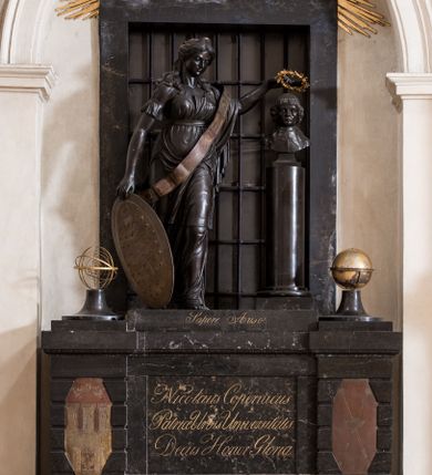 Zdjęcie nr 1: Pomnik przyścienny składa się z wysokiego cokołu, na którym stoi kobieta nakładająca wieniec laurowy na popiersie Mikołaja Kopernika osadzone na kolumnie. Cokół ujęty jest dwoma boniowanymi ryzalitami, z ośmiobocznymi tarczami z herbem Krakowa i Uniwersytetu Krakowskiego. Pośrodku cokołu wyryto inskrypcję: "Nicolaus Copernicus / Patriae Urbis Universisitatis / Decus Honor Gloria". Po bokach na cokole ustawiono na niskich zwężających się, okrągłych w planie cokolikach glob ziemski i sferę planet. Pomiędzy nimi niska płyta z inskrypcją "Sapere Auso". Nad niej stoi kobieta, personifikacja Uranii (?) ukazana w kontrapoście, w szatach ściśle przylegających do ciała i z szarfą przepasaną przez lewe ramię ze znakami zodiaku.  Jej twarz jest owalna, o zaostrzonej brodzie, ostrym nosie i drobnych ustach, otwartych, wydanych oczach, z włosami gęstymi, długimi, falującymi lokami opadającymi na ramiona. Głowa zwieńczona diademem z gwiazdą. Prawą ręką trzyma Tarczę Sobieskiego (z herbem Janina i astrologicznym Bykiem wśród gwiazd) opartą o podłoże, a w lewej wieniec z lauru nad głową Kopernika. Popiersie astronoma jest osadzone na wysokim cokole w kształcie gładkiej kolumny, ukazane frontalnie. Twarz modelowana sumarycznie, z zaznaczonymi zmarszczkami, prostym nosem i kręconymi włosami sięgającymi podbródka. Grupa rzeźbiarska ukazana na tle prostokątnego, zamurowanego przejścia, z kratą. Nad nim złocona gloria z kłębiastymi chmurami, między którymi napis „STA SOL NE MOVERE”. 