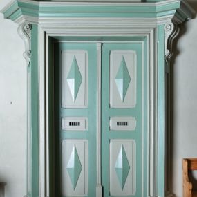 Zdjęcie nr 1: Portal drzwi prostokątnych, prowadzących do kaplicy zakonnej, dwuskrzydłowych, czteropolowych, z romboidalnymi występami został ujęty ukośnie dostawionymi pilastrami z konsolami w miejscu głowic, podtrzymującymi profilowany, mocno wysunięty gzyms. Górna część jest flankowana spływami wolutowymi z kampanulami, zakończonymi rokokowymi wazonami i jest zwieńczona profilowanym gzymsem w kształcie łuku nadwieszonego. W zwieńczeniu owalny obraz w profilowanej, złoconej ramie z wizerunkiem św. Kingi. 
