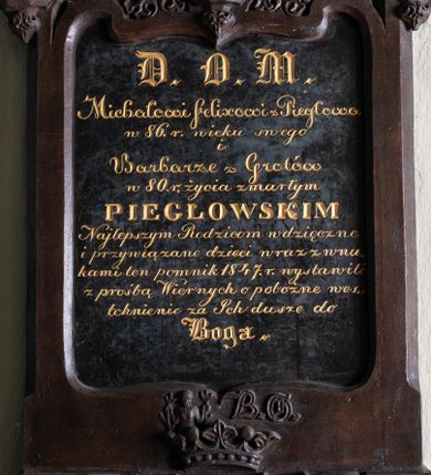 Zdjęcie nr 1: Epitafium utworzone z cokołu, tablicy inskrypcyjnej i dwóch okrągłych portretów zwieńczonych krzyżem. Cokół z czterema arkadkami pod nim i dwiema tarczami z godłami herbów Nałęcz i Rawicz zwieńczonymi koroną. Nad nią klejnot herbu Nałęcz (kobieta z przepaską na czole trzymająca w rękach rogi jelenia) oraz obok niego litery „B. G”. Na tablicy inskrypcja: „D(EO) O(PTIMO) M(AXIMO) / Michałowi Felixowi z Piegłowa / w 86. r(oku) wieku swego / i / Barbarze z Grotów / w 80. r(oku) życia zmarłym / PIEGŁOWSKIM / Najlepszym Rodzicom wdzięczne / i przywiązane dzieci wraz z wnu/kami ten pomnik 1847. r(oku) wystawili / z prośbą Wiernych o pobożne wes/tchnienie za Ich dusze do / Boga”. Nad tablicą okrągłe obrazy z portretami zmarłych, ukazanych w popiersiu. Kobieta o starczej twarzy, długim nosie, otwartych migdałowatych oczach i zaciśniętych ustach, czarnych włosach okrytych prześwitującym czepcem. Ubrana jest w niebieską suknię z niewielkim dekoltem i koronkowym kołnierzem. Mężczyzna ukazany w trzech czwartych, zwrócony w prawo, o wyrazistej twarzy, z długim nosem, otwartymi oczami, zaciśniętymi ustami i z krótkimi brązowymi włosami. Ubrany jest w białą koszulę z wysokim kołnierzem z żabotem oraz czarny płaszcz. Portrety osadzone w profilowanych ramach spiętych od góry łukiem w kształcie oślego grzbietu z żabkami, zwieńczonym krzyżem o ramionach zakończonych stylizowanym astwerkiem.          



