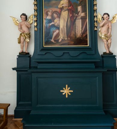 Zdjęcie nr 1: W centralnej części kompozycji ukazany w całej postaci św. Juda Tadeusz, w lekkim kontrapoście, w żółtej szacie i czerwonym płaszczu przepasanym sznurem. Jego prawa dłoń spoczywa na piersi, natomiast w lewej dzierży maczugę. Po lewej stronie obrazu klęczy anioł ubrany w brązową suknię i niebieski płaszcz, w dłoniach trzyma owalny medalion z podobizną Chrystusa (brata stryjecznego Judy Tadeusza) o twarzy podobnej do wizerunku świętego. Po prawej stronie kompozycji jest widoczny wysoki cokół z pozostałościami po dwóch kolumnach; przed cokołem znajdują się drewniane belki oraz kwitnące kwiaty, a za nim fragment palmy. Nad świętym, na tle niebieskiego nieba z różowymi obłokami unoszą się uskrzydlony aniołek z palmą męczeństwa i główki aniołków. 
