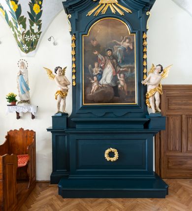 Zdjęcie nr 2: Ołtarz drewniany, jednoosiowy, jednokondygnacyjny. Mensa ołtarza z antepedium, w którym złocony wieniec różany. Nastawa ujęta postumentami z aniołami, w profilowanej ramie z kampanulami po bokach, z uszkami i konsolami w górnej części, zwieńczona bogato profilowanym gzymsem, trójbocznym, z wklęsłymi bokami, z Okiem Opatrzności i muszlą palmetową. Obraz w ramie profilowanej, prostokątny, zamknięty łukiem półkolistym, nadwieszonym; na obrazie przedstawiona Apoteoza św. Jana Nepomucena. Stojące po bokach aniołki w kontrapoście, nagie, z wyciągniętymi rękami, o pulchnych kształtach, przepasane na biodrach złoconymi, marszczonymi draperiami. Nastawy ciemnozielone ze złoconymi ornamentami i profilami; aniołki w naturalistycznej tonacji kolorystycznej. 
