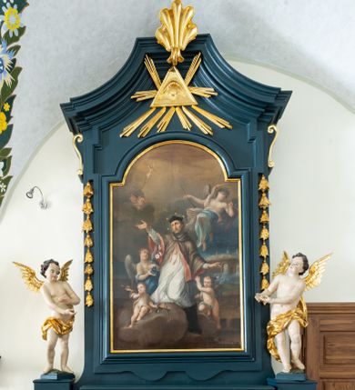 Zdjęcie nr 1: Ołtarz drewniany, jednoosiowy, jednokondygnacyjny. Mensa ołtarza z antepedium, w którym złocony wieniec różany. Nastawa ujęta postumentami z aniołami, w profilowanej ramie z kampanulami po bokach, z uszkami i konsolami w górnej części, zwieńczona bogato profilowanym gzymsem, trójbocznym, z wklęsłymi bokami, z Okiem Opatrzności i muszlą palmetową. Obraz w ramie profilowanej, prostokątny, zamknięty łukiem półkolistym, nadwieszonym; na obrazie przedstawiona Apoteoza św. Jana Nepomucena. Stojące po bokach aniołki w kontrapoście, nagie, z wyciągniętymi rękami, o pulchnych kształtach, przepasane na biodrach złoconymi, marszczonymi draperiami. Nastawy ciemnozielone ze złoconymi ornamentami i profilami; aniołki w naturalistycznej tonacji kolorystycznej. 
