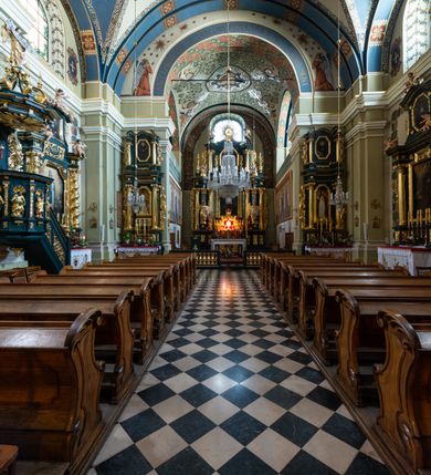 Zdjęcie nr 7: Kościół jest murowany z cegły, tynkowany, jednonawowy. Założony jest na rzucie prostokąta, z czteroprzęsłowym korpusem oraz jednoprzęsłowym prezbiterium, zamknięty prosto i skierowanym na południe. Ściana południowa wychodzi na ogród klasztorny, natomiast wschodnia i północna złączone są z klasztorem. Prezbiterium po obu stronach flankowane jest zakrystiami, nad którymi mieszczą się małe chóry. Chóry otwierają się do pojedynczymi arkadami do prezbiterium z drewnianymi balustradami. Do dwuprzęsłowej nawy od północy przylegają kolejne dwa przęsła korpusu, które stanowią kruchtę i kaplicę klasztoru, a nad nimi wzniesiony jest chór zakonny, oddzielony kratą. Nawa artykułowana jest za pomocą zdwojonych filarów, dźwigających wydatne belkowanie i tworzących półkoliście zamknięte wnęki arkadowe na ołtarze. Korpus kościoła sklepiony jest kolebkowo z lunetami na gurtach, natomiast w prezbiterium i kruchcie znajdują się sklepienia krzyżowe. Ściana arkady tęczowej zamknięta jest półkoliście. Wnętrze kościoła doświetlają umieszczone ponad belkowaniem okna w kształcie stojących prostokątów, zamknięte półkoliście. Do kościoła prowadzą drzwi wejściowe od północy przez kruchtę, do której wejście znajduje się od zachodu przez dziedziniec. Kolejne dwa wejścia prowadzą od strony klasztory przez kruchtę i zakrystię. Fasada północna kościoła wtopiona jest w bryłę klasztoru. Od strony dziedzińca, prowadzącego do głównego wejścia widoczna jest strona zachodnia kościoła, artykułowa zdwojonymi pilastrami. Portal główny flankowany jest kolumnami na tle pilastrów, które podtrzymują belkowanie i przerwany półkoliście zamknięty przyczółek. Podpory wsparte są na wysokich cokołach. Drzwi wejściowe flankuje półkoliście zamknięta arkada wsparta na parze filarów. Kościół nakrywa dach siodłowy, nad drugim przęsłem korpusu od strony północnej znajduje się wieżyczka na sygnaturkę ze zdwojoną latarnią. Przed kościołem znajduje się dziedziniec oddzielony od ulicy klasycystycznym murem z bramą.