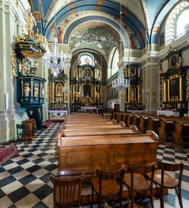 Zdjęcie nr 13: Kościół jest murowany z cegły, tynkowany, jednonawowy. Założony jest na rzucie prostokąta, z czteroprzęsłowym korpusem oraz jednoprzęsłowym prezbiterium, zamknięty prosto i skierowanym na południe. Ściana południowa wychodzi na ogród klasztorny, natomiast wschodnia i północna złączone są z klasztorem. Prezbiterium po obu stronach flankowane jest zakrystiami, nad którymi mieszczą się małe chóry. Chóry otwierają się do pojedynczymi arkadami do prezbiterium z drewnianymi balustradami. Do dwuprzęsłowej nawy od północy przylegają kolejne dwa przęsła korpusu, które stanowią kruchtę i kaplicę klasztoru, a nad nimi wzniesiony jest chór zakonny, oddzielony kratą. Nawa artykułowana jest za pomocą zdwojonych filarów, dźwigających wydatne belkowanie i tworzących półkoliście zamknięte wnęki arkadowe na ołtarze. Korpus kościoła sklepiony jest kolebkowo z lunetami na gurtach, natomiast w prezbiterium i kruchcie znajdują się sklepienia krzyżowe. Ściana arkady tęczowej zamknięta jest półkoliście. Wnętrze kościoła doświetlają umieszczone ponad belkowaniem okna w kształcie stojących prostokątów, zamknięte półkoliście. Do kościoła prowadzą drzwi wejściowe od północy przez kruchtę, do której wejście znajduje się od zachodu przez dziedziniec. Kolejne dwa wejścia prowadzą od strony klasztory przez kruchtę i zakrystię. Fasada północna kościoła wtopiona jest w bryłę klasztoru. Od strony dziedzińca, prowadzącego do głównego wejścia widoczna jest strona zachodnia kościoła, artykułowa zdwojonymi pilastrami. Portal główny flankowany jest kolumnami na tle pilastrów, które podtrzymują belkowanie i przerwany półkoliście zamknięty przyczółek. Podpory wsparte są na wysokich cokołach. Drzwi wejściowe flankuje półkoliście zamknięta arkada wsparta na parze filarów. Kościół nakrywa dach siodłowy, nad drugim przęsłem korpusu od strony północnej znajduje się wieżyczka na sygnaturkę ze zdwojoną latarnią. Przed kościołem znajduje się dziedziniec oddzielony od ulicy klasycystycznym murem z bramą.