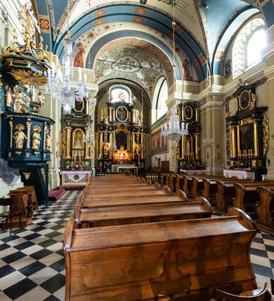 Zdjęcie nr 10: Kościół jest murowany z cegły, tynkowany, jednonawowy. Założony jest na rzucie prostokąta, z czteroprzęsłowym korpusem oraz jednoprzęsłowym prezbiterium, zamknięty prosto i skierowanym na południe. Ściana południowa wychodzi na ogród klasztorny, natomiast wschodnia i północna złączone są z klasztorem. Prezbiterium po obu stronach flankowane jest zakrystiami, nad którymi mieszczą się małe chóry. Chóry otwierają się do pojedynczymi arkadami do prezbiterium z drewnianymi balustradami. Do dwuprzęsłowej nawy od północy przylegają kolejne dwa przęsła korpusu, które stanowią kruchtę i kaplicę klasztoru, a nad nimi wzniesiony jest chór zakonny, oddzielony kratą. Nawa artykułowana jest za pomocą zdwojonych filarów, dźwigających wydatne belkowanie i tworzących półkoliście zamknięte wnęki arkadowe na ołtarze. Korpus kościoła sklepiony jest kolebkowo z lunetami na gurtach, natomiast w prezbiterium i kruchcie znajdują się sklepienia krzyżowe. Ściana arkady tęczowej zamknięta jest półkoliście. Wnętrze kościoła doświetlają umieszczone ponad belkowaniem okna w kształcie stojących prostokątów, zamknięte półkoliście. Do kościoła prowadzą drzwi wejściowe od północy przez kruchtę, do której wejście znajduje się od zachodu przez dziedziniec. Kolejne dwa wejścia prowadzą od strony klasztory przez kruchtę i zakrystię. Fasada północna kościoła wtopiona jest w bryłę klasztoru. Od strony dziedzińca, prowadzącego do głównego wejścia widoczna jest strona zachodnia kościoła, artykułowa zdwojonymi pilastrami. Portal główny flankowany jest kolumnami na tle pilastrów, które podtrzymują belkowanie i przerwany półkoliście zamknięty przyczółek. Podpory wsparte są na wysokich cokołach. Drzwi wejściowe flankuje półkoliście zamknięta arkada wsparta na parze filarów. Kościół nakrywa dach siodłowy, nad drugim przęsłem korpusu od strony północnej znajduje się wieżyczka na sygnaturkę ze zdwojoną latarnią. Przed kościołem znajduje się dziedziniec oddzielony od ulicy klasycystycznym murem z bramą.