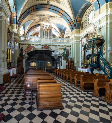 Zdjęcie nr 9: Kościół jest murowany z cegły, tynkowany, jednonawowy. Założony jest na rzucie prostokąta, z czteroprzęsłowym korpusem oraz jednoprzęsłowym prezbiterium, zamknięty prosto i skierowanym na południe. Ściana południowa wychodzi na ogród klasztorny, natomiast wschodnia i północna złączone są z klasztorem. Prezbiterium po obu stronach flankowane jest zakrystiami, nad którymi mieszczą się małe chóry. Chóry otwierają się do pojedynczymi arkadami do prezbiterium z drewnianymi balustradami. Do dwuprzęsłowej nawy od północy przylegają kolejne dwa przęsła korpusu, które stanowią kruchtę i kaplicę klasztoru, a nad nimi wzniesiony jest chór zakonny, oddzielony kratą. Nawa artykułowana jest za pomocą zdwojonych filarów, dźwigających wydatne belkowanie i tworzących półkoliście zamknięte wnęki arkadowe na ołtarze. Korpus kościoła sklepiony jest kolebkowo z lunetami na gurtach, natomiast w prezbiterium i kruchcie znajdują się sklepienia krzyżowe. Ściana arkady tęczowej zamknięta jest półkoliście. Wnętrze kościoła doświetlają umieszczone ponad belkowaniem okna w kształcie stojących prostokątów, zamknięte półkoliście. Do kościoła prowadzą drzwi wejściowe od północy przez kruchtę, do której wejście znajduje się od zachodu przez dziedziniec. Kolejne dwa wejścia prowadzą od strony klasztory przez kruchtę i zakrystię. Fasada północna kościoła wtopiona jest w bryłę klasztoru. Od strony dziedzińca, prowadzącego do głównego wejścia widoczna jest strona zachodnia kościoła, artykułowa zdwojonymi pilastrami. Portal główny flankowany jest kolumnami na tle pilastrów, które podtrzymują belkowanie i przerwany półkoliście zamknięty przyczółek. Podpory wsparte są na wysokich cokołach. Drzwi wejściowe flankuje półkoliście zamknięta arkada wsparta na parze filarów. Kościół nakrywa dach siodłowy, nad drugim przęsłem korpusu od strony północnej znajduje się wieżyczka na sygnaturkę ze zdwojoną latarnią. Przed kościołem znajduje się dziedziniec oddzielony od ulicy klasycystycznym murem z bramą.