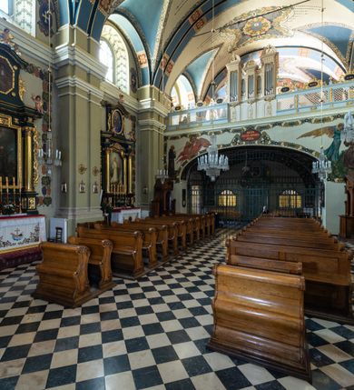 Zdjęcie nr 12: Kościół jest murowany z cegły, tynkowany, jednonawowy. Założony jest na rzucie prostokąta, z czteroprzęsłowym korpusem oraz jednoprzęsłowym prezbiterium, zamknięty prosto i skierowanym na południe. Ściana południowa wychodzi na ogród klasztorny, natomiast wschodnia i północna złączone są z klasztorem. Prezbiterium po obu stronach flankowane jest zakrystiami, nad którymi mieszczą się małe chóry. Chóry otwierają się do pojedynczymi arkadami do prezbiterium z drewnianymi balustradami. Do dwuprzęsłowej nawy od północy przylegają kolejne dwa przęsła korpusu, które stanowią kruchtę i kaplicę klasztoru, a nad nimi wzniesiony jest chór zakonny, oddzielony kratą. Nawa artykułowana jest za pomocą zdwojonych filarów, dźwigających wydatne belkowanie i tworzących półkoliście zamknięte wnęki arkadowe na ołtarze. Korpus kościoła sklepiony jest kolebkowo z lunetami na gurtach, natomiast w prezbiterium i kruchcie znajdują się sklepienia krzyżowe. Ściana arkady tęczowej zamknięta jest półkoliście. Wnętrze kościoła doświetlają umieszczone ponad belkowaniem okna w kształcie stojących prostokątów, zamknięte półkoliście. Do kościoła prowadzą drzwi wejściowe od północy przez kruchtę, do której wejście znajduje się od zachodu przez dziedziniec. Kolejne dwa wejścia prowadzą od strony klasztory przez kruchtę i zakrystię. Fasada północna kościoła wtopiona jest w bryłę klasztoru. Od strony dziedzińca, prowadzącego do głównego wejścia widoczna jest strona zachodnia kościoła, artykułowa zdwojonymi pilastrami. Portal główny flankowany jest kolumnami na tle pilastrów, które podtrzymują belkowanie i przerwany półkoliście zamknięty przyczółek. Podpory wsparte są na wysokich cokołach. Drzwi wejściowe flankuje półkoliście zamknięta arkada wsparta na parze filarów. Kościół nakrywa dach siodłowy, nad drugim przęsłem korpusu od strony północnej znajduje się wieżyczka na sygnaturkę ze zdwojoną latarnią. Przed kościołem znajduje się dziedziniec oddzielony od ulicy klasycystycznym murem z bramą.