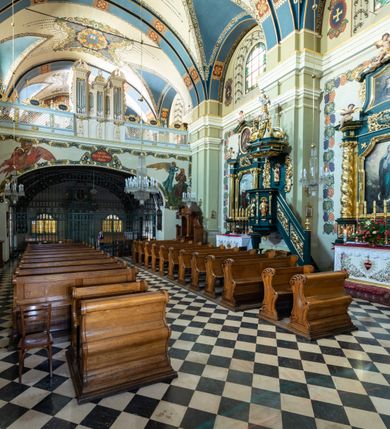 Zdjęcie nr 11: Kościół jest murowany z cegły, tynkowany, jednonawowy. Założony jest na rzucie prostokąta, z czteroprzęsłowym korpusem oraz jednoprzęsłowym prezbiterium, zamknięty prosto i skierowanym na południe. Ściana południowa wychodzi na ogród klasztorny, natomiast wschodnia i północna złączone są z klasztorem. Prezbiterium po obu stronach flankowane jest zakrystiami, nad którymi mieszczą się małe chóry. Chóry otwierają się do pojedynczymi arkadami do prezbiterium z drewnianymi balustradami. Do dwuprzęsłowej nawy od północy przylegają kolejne dwa przęsła korpusu, które stanowią kruchtę i kaplicę klasztoru, a nad nimi wzniesiony jest chór zakonny, oddzielony kratą. Nawa artykułowana jest za pomocą zdwojonych filarów, dźwigających wydatne belkowanie i tworzących półkoliście zamknięte wnęki arkadowe na ołtarze. Korpus kościoła sklepiony jest kolebkowo z lunetami na gurtach, natomiast w prezbiterium i kruchcie znajdują się sklepienia krzyżowe. Ściana arkady tęczowej zamknięta jest półkoliście. Wnętrze kościoła doświetlają umieszczone ponad belkowaniem okna w kształcie stojących prostokątów, zamknięte półkoliście. Do kościoła prowadzą drzwi wejściowe od północy przez kruchtę, do której wejście znajduje się od zachodu przez dziedziniec. Kolejne dwa wejścia prowadzą od strony klasztory przez kruchtę i zakrystię. Fasada północna kościoła wtopiona jest w bryłę klasztoru. Od strony dziedzińca, prowadzącego do głównego wejścia widoczna jest strona zachodnia kościoła, artykułowa zdwojonymi pilastrami. Portal główny flankowany jest kolumnami na tle pilastrów, które podtrzymują belkowanie i przerwany półkoliście zamknięty przyczółek. Podpory wsparte są na wysokich cokołach. Drzwi wejściowe flankuje półkoliście zamknięta arkada wsparta na parze filarów. Kościół nakrywa dach siodłowy, nad drugim przęsłem korpusu od strony północnej znajduje się wieżyczka na sygnaturkę ze zdwojoną latarnią. Przed kościołem znajduje się dziedziniec oddzielony od ulicy klasycystycznym murem z bramą.