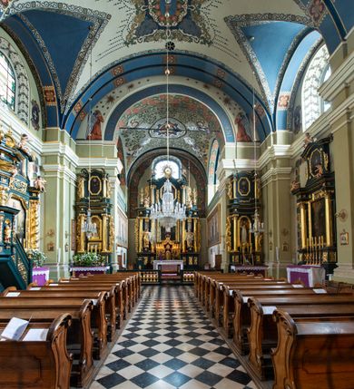 Zdjęcie nr 19: Kościół jest murowany z cegły, tynkowany, jednonawowy. Założony jest na rzucie prostokąta, z czteroprzęsłowym korpusem oraz jednoprzęsłowym prezbiterium, zamknięty prosto i skierowanym na południe. Ściana południowa wychodzi na ogród klasztorny, natomiast wschodnia i północna złączone są z klasztorem. Prezbiterium po obu stronach flankowane jest zakrystiami, nad którymi mieszczą się małe chóry. Chóry otwierają się do pojedynczymi arkadami do prezbiterium z drewnianymi balustradami. Do dwuprzęsłowej nawy od północy przylegają kolejne dwa przęsła korpusu, które stanowią kruchtę i kaplicę klasztoru, a nad nimi wzniesiony jest chór zakonny, oddzielony kratą. Nawa artykułowana jest za pomocą zdwojonych filarów, dźwigających wydatne belkowanie i tworzących półkoliście zamknięte wnęki arkadowe na ołtarze. Korpus kościoła sklepiony jest kolebkowo z lunetami na gurtach, natomiast w prezbiterium i kruchcie znajdują się sklepienia krzyżowe. Ściana arkady tęczowej zamknięta jest półkoliście. Wnętrze kościoła doświetlają umieszczone ponad belkowaniem okna w kształcie stojących prostokątów, zamknięte półkoliście. Do kościoła prowadzą drzwi wejściowe od północy przez kruchtę, do której wejście znajduje się od zachodu przez dziedziniec. Kolejne dwa wejścia prowadzą od strony klasztory przez kruchtę i zakrystię. Fasada północna kościoła wtopiona jest w bryłę klasztoru. Od strony dziedzińca, prowadzącego do głównego wejścia widoczna jest strona zachodnia kościoła, artykułowa zdwojonymi pilastrami. Portal główny flankowany jest kolumnami na tle pilastrów, które podtrzymują belkowanie i przerwany półkoliście zamknięty przyczółek. Podpory wsparte są na wysokich cokołach. Drzwi wejściowe flankuje półkoliście zamknięta arkada wsparta na parze filarów. Kościół nakrywa dach siodłowy, nad drugim przęsłem korpusu od strony północnej znajduje się wieżyczka na sygnaturkę ze zdwojoną latarnią. Przed kościołem znajduje się dziedziniec oddzielony od ulicy klasycystycznym murem z bramą.