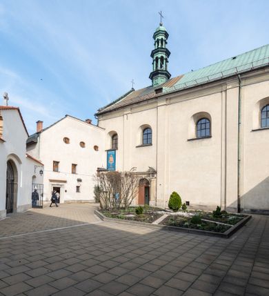 Zdjęcie nr 1: Kościół jest murowany z cegły, tynkowany, jednonawowy. Założony jest na rzucie prostokąta, z czteroprzęsłowym korpusem oraz jednoprzęsłowym prezbiterium, zamknięty prosto i skierowanym na południe. Ściana południowa wychodzi na ogród klasztorny, natomiast wschodnia i północna złączone są z klasztorem. Prezbiterium po obu stronach flankowane jest zakrystiami, nad którymi mieszczą się małe chóry. Chóry otwierają się do pojedynczymi arkadami do prezbiterium z drewnianymi balustradami. Do dwuprzęsłowej nawy od północy przylegają kolejne dwa przęsła korpusu, które stanowią kruchtę i kaplicę klasztoru, a nad nimi wzniesiony jest chór zakonny, oddzielony kratą. Nawa artykułowana jest za pomocą zdwojonych filarów, dźwigających wydatne belkowanie i tworzących półkoliście zamknięte wnęki arkadowe na ołtarze. Korpus kościoła sklepiony jest kolebkowo z lunetami na gurtach, natomiast w prezbiterium i kruchcie znajdują się sklepienia krzyżowe. Ściana arkady tęczowej zamknięta jest półkoliście. Wnętrze kościoła doświetlają umieszczone ponad belkowaniem okna w kształcie stojących prostokątów, zamknięte półkoliście. Do kościoła prowadzą drzwi wejściowe od północy przez kruchtę, do której wejście znajduje się od zachodu przez dziedziniec. Kolejne dwa wejścia prowadzą od strony klasztory przez kruchtę i zakrystię. Fasada północna kościoła wtopiona jest w bryłę klasztoru. Od strony dziedzińca, prowadzącego do głównego wejścia widoczna jest strona zachodnia kościoła, artykułowa zdwojonymi pilastrami. Portal główny flankowany jest kolumnami na tle pilastrów, które podtrzymują belkowanie i przerwany półkoliście zamknięty przyczółek. Podpory wsparte są na wysokich cokołach. Drzwi wejściowe flankuje półkoliście zamknięta arkada wsparta na parze filarów. Kościół nakrywa dach siodłowy, nad drugim przęsłem korpusu od strony północnej znajduje się wieżyczka na sygnaturkę ze zdwojoną latarnią. Przed kościołem znajduje się dziedziniec oddzielony od ulicy klasycystycznym murem z bramą.