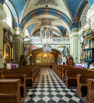 Zdjęcie nr 20: Kościół jest murowany z cegły, tynkowany, jednonawowy. Założony jest na rzucie prostokąta, z czteroprzęsłowym korpusem oraz jednoprzęsłowym prezbiterium, zamknięty prosto i skierowanym na południe. Ściana południowa wychodzi na ogród klasztorny, natomiast wschodnia i północna złączone są z klasztorem. Prezbiterium po obu stronach flankowane jest zakrystiami, nad którymi mieszczą się małe chóry. Chóry otwierają się do pojedynczymi arkadami do prezbiterium z drewnianymi balustradami. Do dwuprzęsłowej nawy od północy przylegają kolejne dwa przęsła korpusu, które stanowią kruchtę i kaplicę klasztoru, a nad nimi wzniesiony jest chór zakonny, oddzielony kratą. Nawa artykułowana jest za pomocą zdwojonych filarów, dźwigających wydatne belkowanie i tworzących półkoliście zamknięte wnęki arkadowe na ołtarze. Korpus kościoła sklepiony jest kolebkowo z lunetami na gurtach, natomiast w prezbiterium i kruchcie znajdują się sklepienia krzyżowe. Ściana arkady tęczowej zamknięta jest półkoliście. Wnętrze kościoła doświetlają umieszczone ponad belkowaniem okna w kształcie stojących prostokątów, zamknięte półkoliście. Do kościoła prowadzą drzwi wejściowe od północy przez kruchtę, do której wejście znajduje się od zachodu przez dziedziniec. Kolejne dwa wejścia prowadzą od strony klasztory przez kruchtę i zakrystię. Fasada północna kościoła wtopiona jest w bryłę klasztoru. Od strony dziedzińca, prowadzącego do głównego wejścia widoczna jest strona zachodnia kościoła, artykułowa zdwojonymi pilastrami. Portal główny flankowany jest kolumnami na tle pilastrów, które podtrzymują belkowanie i przerwany półkoliście zamknięty przyczółek. Podpory wsparte są na wysokich cokołach. Drzwi wejściowe flankuje półkoliście zamknięta arkada wsparta na parze filarów. Kościół nakrywa dach siodłowy, nad drugim przęsłem korpusu od strony północnej znajduje się wieżyczka na sygnaturkę ze zdwojoną latarnią. Przed kościołem znajduje się dziedziniec oddzielony od ulicy klasycystycznym murem z bramą.