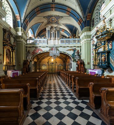 Zdjęcie nr 21: Kościół jest murowany z cegły, tynkowany, jednonawowy. Założony jest na rzucie prostokąta, z czteroprzęsłowym korpusem oraz jednoprzęsłowym prezbiterium, zamknięty prosto i skierowanym na południe. Ściana południowa wychodzi na ogród klasztorny, natomiast wschodnia i północna złączone są z klasztorem. Prezbiterium po obu stronach flankowane jest zakrystiami, nad którymi mieszczą się małe chóry. Chóry otwierają się do pojedynczymi arkadami do prezbiterium z drewnianymi balustradami. Do dwuprzęsłowej nawy od północy przylegają kolejne dwa przęsła korpusu, które stanowią kruchtę i kaplicę klasztoru, a nad nimi wzniesiony jest chór zakonny, oddzielony kratą. Nawa artykułowana jest za pomocą zdwojonych filarów, dźwigających wydatne belkowanie i tworzących półkoliście zamknięte wnęki arkadowe na ołtarze. Korpus kościoła sklepiony jest kolebkowo z lunetami na gurtach, natomiast w prezbiterium i kruchcie znajdują się sklepienia krzyżowe. Ściana arkady tęczowej zamknięta jest półkoliście. Wnętrze kościoła doświetlają umieszczone ponad belkowaniem okna w kształcie stojących prostokątów, zamknięte półkoliście. Do kościoła prowadzą drzwi wejściowe od północy przez kruchtę, do której wejście znajduje się od zachodu przez dziedziniec. Kolejne dwa wejścia prowadzą od strony klasztory przez kruchtę i zakrystię. Fasada północna kościoła wtopiona jest w bryłę klasztoru. Od strony dziedzińca, prowadzącego do głównego wejścia widoczna jest strona zachodnia kościoła, artykułowa zdwojonymi pilastrami. Portal główny flankowany jest kolumnami na tle pilastrów, które podtrzymują belkowanie i przerwany półkoliście zamknięty przyczółek. Podpory wsparte są na wysokich cokołach. Drzwi wejściowe flankuje półkoliście zamknięta arkada wsparta na parze filarów. Kościół nakrywa dach siodłowy, nad drugim przęsłem korpusu od strony północnej znajduje się wieżyczka na sygnaturkę ze zdwojoną latarnią. Przed kościołem znajduje się dziedziniec oddzielony od ulicy klasycystycznym murem z bramą.