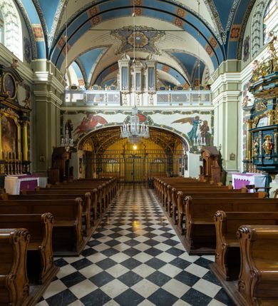 Zdjęcie nr 24: Kościół jest murowany z cegły, tynkowany, jednonawowy. Założony jest na rzucie prostokąta, z czteroprzęsłowym korpusem oraz jednoprzęsłowym prezbiterium, zamknięty prosto i skierowanym na południe. Ściana południowa wychodzi na ogród klasztorny, natomiast wschodnia i północna złączone są z klasztorem. Prezbiterium po obu stronach flankowane jest zakrystiami, nad którymi mieszczą się małe chóry. Chóry otwierają się do pojedynczymi arkadami do prezbiterium z drewnianymi balustradami. Do dwuprzęsłowej nawy od północy przylegają kolejne dwa przęsła korpusu, które stanowią kruchtę i kaplicę klasztoru, a nad nimi wzniesiony jest chór zakonny, oddzielony kratą. Nawa artykułowana jest za pomocą zdwojonych filarów, dźwigających wydatne belkowanie i tworzących półkoliście zamknięte wnęki arkadowe na ołtarze. Korpus kościoła sklepiony jest kolebkowo z lunetami na gurtach, natomiast w prezbiterium i kruchcie znajdują się sklepienia krzyżowe. Ściana arkady tęczowej zamknięta jest półkoliście. Wnętrze kościoła doświetlają umieszczone ponad belkowaniem okna w kształcie stojących prostokątów, zamknięte półkoliście. Do kościoła prowadzą drzwi wejściowe od północy przez kruchtę, do której wejście znajduje się od zachodu przez dziedziniec. Kolejne dwa wejścia prowadzą od strony klasztory przez kruchtę i zakrystię. Fasada północna kościoła wtopiona jest w bryłę klasztoru. Od strony dziedzińca, prowadzącego do głównego wejścia widoczna jest strona zachodnia kościoła, artykułowa zdwojonymi pilastrami. Portal główny flankowany jest kolumnami na tle pilastrów, które podtrzymują belkowanie i przerwany półkoliście zamknięty przyczółek. Podpory wsparte są na wysokich cokołach. Drzwi wejściowe flankuje półkoliście zamknięta arkada wsparta na parze filarów. Kościół nakrywa dach siodłowy, nad drugim przęsłem korpusu od strony północnej znajduje się wieżyczka na sygnaturkę ze zdwojoną latarnią. Przed kościołem znajduje się dziedziniec oddzielony od ulicy klasycystycznym murem z bramą.