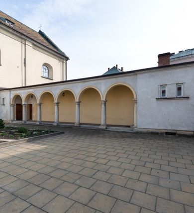 Zdjęcie nr 3: Kościół jest murowany z cegły, tynkowany, jednonawowy. Założony jest na rzucie prostokąta, z czteroprzęsłowym korpusem oraz jednoprzęsłowym prezbiterium, zamknięty prosto i skierowanym na południe. Ściana południowa wychodzi na ogród klasztorny, natomiast wschodnia i północna złączone są z klasztorem. Prezbiterium po obu stronach flankowane jest zakrystiami, nad którymi mieszczą się małe chóry. Chóry otwierają się do pojedynczymi arkadami do prezbiterium z drewnianymi balustradami. Do dwuprzęsłowej nawy od północy przylegają kolejne dwa przęsła korpusu, które stanowią kruchtę i kaplicę klasztoru, a nad nimi wzniesiony jest chór zakonny, oddzielony kratą. Nawa artykułowana jest za pomocą zdwojonych filarów, dźwigających wydatne belkowanie i tworzących półkoliście zamknięte wnęki arkadowe na ołtarze. Korpus kościoła sklepiony jest kolebkowo z lunetami na gurtach, natomiast w prezbiterium i kruchcie znajdują się sklepienia krzyżowe. Ściana arkady tęczowej zamknięta jest półkoliście. Wnętrze kościoła doświetlają umieszczone ponad belkowaniem okna w kształcie stojących prostokątów, zamknięte półkoliście. Do kościoła prowadzą drzwi wejściowe od północy przez kruchtę, do której wejście znajduje się od zachodu przez dziedziniec. Kolejne dwa wejścia prowadzą od strony klasztory przez kruchtę i zakrystię. Fasada północna kościoła wtopiona jest w bryłę klasztoru. Od strony dziedzińca, prowadzącego do głównego wejścia widoczna jest strona zachodnia kościoła, artykułowa zdwojonymi pilastrami. Portal główny flankowany jest kolumnami na tle pilastrów, które podtrzymują belkowanie i przerwany półkoliście zamknięty przyczółek. Podpory wsparte są na wysokich cokołach. Drzwi wejściowe flankuje półkoliście zamknięta arkada wsparta na parze filarów. Kościół nakrywa dach siodłowy, nad drugim przęsłem korpusu od strony północnej znajduje się wieżyczka na sygnaturkę ze zdwojoną latarnią. Przed kościołem znajduje się dziedziniec oddzielony od ulicy klasycystycznym murem z bramą.