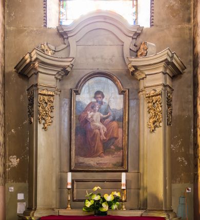 Zdjęcie nr 1: Ołtarz architektoniczny, drewniany, jednoosiowy, jednokondygnacyjny ze zwieńczeniem. Profilowana mensa w typie sarkofagowym na niskim, prostopadłym cokole, zakończona gzymsem. Część środkowa nastawy ujęta dwoma wklęsłowypukłymi, opilastrowanymi, ustawionymi skośnie podporami zwieńczonymi fragmentami pełnego belkowania z wydatnym gzymsem.
Trzony pilastrów zdobione u góry nakładanym ornamentem rocaille'owym. W polu centralnym prostokątna płycina ze złoconą ramą, nad nią prostokątny obraz, zamknięty łukiem nadwieszonym z uskokiem przedstawiający św. Józefa z Dzieciątkiem. Zwieńczenie zakończone gzymsem w kształcie łuku wklęsło-wypukłego, flankowane spływami dekorowanymi ornamentem rocaille’owym. Struktura polichromowana na kolor szary, profile i ornamenty złocone. 