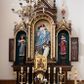 Zdjęcie nr 1: Ołtarz architektoniczny, jednokondygnacyjny, trójosiowy. Mensa prostopadłościenna z kamiennym portatylem. Antepedium dekorowane trzema prostokątnymi płycinami, boczne z aplikowanymi rozetkami, środkowa z monogramem maryjnym. Tabernakulum w formie prostopadłościennej szafki ujętej złoconymi kolumienkami podtrzymującymi łuk półkolisty, powyżej gzyms w kształcie nadwieszonego łuku, zwieńczony ażurowym  ornamentem roślinnym. Na drzwiczkach płaskorzeźbiony kielich z hostią. Retabulum ustawione na wysokim cokole i predelli. W predelli, pod niszami bocznymi płyciny z rzeźbionymi główkami anielskimi. Oś środkowa wyższa i szersza w formie półkolistej arkady podtrzymywanej przez parę wąskich kolumienek o kostkowych kapitelach z trójkątnym tympanonem. W polu środkowym wnęka z polichromowaną płaskorzeźbą przedstawiającą Matkę Boską Różańcową ze św. Dominikiem. Poniżej napis: „MATKO. BOŻA. MÓDL. SIĘ. ZA. NAMI”. Po bokach tympanonu na wysokich cokołach ustawione dwie rzeźby aniołów ze skrzydłami skierowanymi ku górze; w polu uskrzydlona główka aniołka, gzyms dekorowany wicią roślinną. Osie boczne o konstrukcji i zdobnictwie analogicznym jak oś główna. W niszach ustawione są pełnoplastyczne figury św. Kazimierza Jagiellończyka po lewej stronie oraz św. Alojzego Gonzagi po prawej stronie. Zwieńczenie ołtarza w formie niewielkiej aediculi z baldachimem, nakrytej kopułą z zatkniętym na szczycie krzyżem. Pod baldachimem dwie słabowidoczne rzeźby świętych. Całość struktury ołtarza bejcowana i lakierowana w kolorze ciemnobrązowym, wnęki boczne ciemnoniebieskie, detal architektoniczny i profilowania pozłacane.
