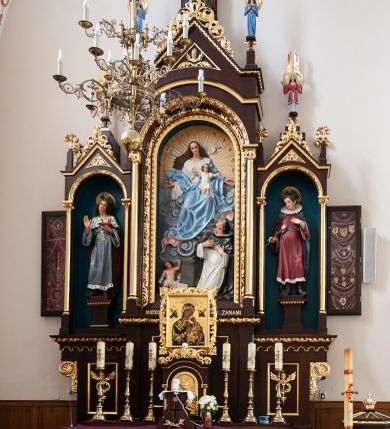 Zdjęcie nr 1: Ołtarz architektoniczny, jednokondygnacyjny, trójosiowy. Mensa prostopadłościenna z kamiennym portatylem. Antepedium dekorowane trzema prostokątnymi płycinami, boczne z aplikowanymi rozetkami, środkowa z monogramem maryjnym. Tabernakulum w formie prostopadłościennej szafki ujętej złoconymi kolumienkami podtrzymującymi łuk półkolisty, powyżej gzyms w kształcie nadwieszonego łuku, zwieńczony ażurowym  ornamentem roślinnym. Na drzwiczkach płaskorzeźbiony kielich z hostią. Retabulum ustawione na wysokim cokole i predelli. W predelli, pod niszami bocznymi płyciny z rzeźbionymi główkami anielskimi. Oś środkowa wyższa i szersza w formie półkolistej arkady podtrzymywanej przez parę wąskich kolumienek o kostkowych kapitelach z trójkątnym tympanonem. W polu środkowym wnęka z polichromowaną płaskorzeźbą przedstawiającą Matkę Boską Różańcową ze św. Dominikiem. Poniżej napis: „MATKO. BOŻA. MÓDL. SIĘ. ZA. NAMI”. Po bokach tympanonu na wysokich cokołach ustawione dwie rzeźby aniołów ze skrzydłami skierowanymi ku górze; w polu uskrzydlona główka aniołka, gzyms dekorowany wicią roślinną. Osie boczne o konstrukcji i zdobnictwie analogicznym jak oś główna. W niszach ustawione są pełnoplastyczne figury św. Kazimierza Jagiellończyka po lewej stronie oraz św. Alojzego Gonzagi po prawej stronie. Zwieńczenie ołtarza w formie niewielkiej aediculi z baldachimem, nakrytej kopułą z zatkniętym na szczycie krzyżem. Pod baldachimem dwie słabowidoczne rzeźby świętych. Całość struktury ołtarza bejcowana i lakierowana w kolorze ciemnobrązowym, wnęki boczne ciemnoniebieskie, detal architektoniczny i profilowania pozłacane.
