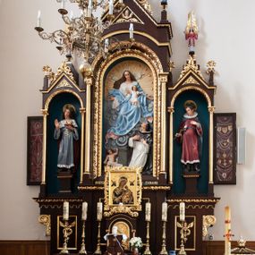 Zdjęcie nr 1: Ołtarz architektoniczny, jednokondygnacyjny, trójosiowy. Mensa prostopadłościenna z kamiennym portatylem. Antepedium dekorowane trzema prostokątnymi płycinami, boczne z aplikowanymi rozetkami, środkowa z monogramem maryjnym. Tabernakulum w formie prostopadłościennej szafki ujętej złoconymi kolumienkami podtrzymującymi łuk półkolisty, powyżej gzyms w kształcie nadwieszonego łuku, zwieńczony ażurowym  ornamentem roślinnym. Na drzwiczkach płaskorzeźbiony kielich z hostią. Retabulum ustawione na wysokim cokole i predelli. W predelli, pod niszami bocznymi płyciny z rzeźbionymi główkami anielskimi. Oś środkowa wyższa i szersza w formie półkolistej arkady podtrzymywanej przez parę wąskich kolumienek o kostkowych kapitelach z trójkątnym tympanonem. W polu środkowym wnęka z polichromowaną płaskorzeźbą przedstawiającą Matkę Boską Różańcową ze św. Dominikiem. Poniżej napis: „MATKO. BOŻA. MÓDL. SIĘ. ZA. NAMI”. Po bokach tympanonu na wysokich cokołach ustawione dwie rzeźby aniołów ze skrzydłami skierowanymi ku górze; w polu uskrzydlona główka aniołka, gzyms dekorowany wicią roślinną. Osie boczne o konstrukcji i zdobnictwie analogicznym jak oś główna. W niszach ustawione są pełnoplastyczne figury św. Kazimierza Jagiellończyka po lewej stronie oraz św. Alojzego Gonzagi po prawej stronie. Zwieńczenie ołtarza w formie niewielkiej aediculi z baldachimem, nakrytej kopułą z zatkniętym na szczycie krzyżem. Pod baldachimem dwie słabowidoczne rzeźby świętych. Całość struktury ołtarza bejcowana i lakierowana w kolorze ciemnobrązowym, wnęki boczne ciemnoniebieskie, detal architektoniczny i profilowania pozłacane.
