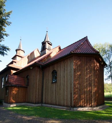 Zdjęcie nr 2: Kościół drewniany na podmurówce z kamienia, o konstrukcji zrębowej, szalowany; jednonawowy, orientowany; wieża o konstrukcji słupowej.
Prezbiterium na planie prostokąta zamkniętego trójbocznie, od północy przylega prostokątna w rzucie zakrystia; nawa na planie prostokąta, z przylegającą od południa kruchtą na rzucie kwadratu; dobudowana nawa na planie dłuższego od poprzedniej prostokąta, od zachodu wieża na planie kwadratu, częściowo wtopiona w ścianę zamykającą nawę, z wyodrębnionymi dwoma pomieszczeniami flankującymi ją.
Nawy i prezbiterium nakryte stropami, oddzielone od siebie szerokimi arkadami zamkniętymi łukami odcinkowymi. W zachodniej części większej nawy prosty parapet chóru muzycznego wsparty na dwóch drewnianych filarach; prospekt organowy przepruwa strop w przestrzeń wieży. Posadzka z płyt ceramicznych. Otwory okienne w formie stojącego prostokąta zamkniętego łukiem półkolistym, obwiedzione listwowymi opaskami, z kwaterowymi podziałami; od strony południowej – jedno w prezbiterium i po dwa w każdej części nawy, od strony północnej po dwa w każdej części nawy, od zachodniej dwa niewielkie flankujące wieżę. W zakrystii analogiczny otwór okienny od wschodu i mniejszy od północy. Otwory wejściowe: z prezbiterium do zakrystii drzwi płycinowe w futrynie; w przejściu z mniejszej nawy do kruchty drzwi płycinowe w futrynie; w przejściu z przyziemia wieży do większej nawy otwór w formie stojącego prostokąta z wklęsłymi górnymi narożami, obwiedziony listwowymi opaskami. 
Ściany z zewnątrz szalowane z listwowaniem. Trzy dachy z osobnymi kalenicami, nad prezbiterium wielospadowy; nad dwiema nawami dwuspadowe, zakończone daszkami okapowymi; kryte ceramiczną dachówką. Wieżyczka na sygnaturkę na kalenicy nad mniejszą nawą, obita blachą, zamknięta daszkiem wieżowym. 
Wieża o ścianach zwężających się ku górze, trójkondygnacyjna. Dolna kondygnacja zamknięta gzymsem, a dwie wyższe daszkami okapowymi. Całość zwieńczona hełmem ostrosłupowym z latarnią przeprutą oknami. Otwory okienne: w pierwszej kondygnacji na ścianie wschodniej i zachodniej w formie stojącego prostokąta zamkniętego łukiem półkolistym, obwiedzione listwowymi opaskami, z kwaterowymi podziałami; w drugiej kondygnacji z trzech stron okulusy, w trzeciej z czterech stron niewielkie okienka. Otwór wejściowy od zachodu, na pięciu kamiennych stopniach, drzwi deskowe-spągowe, dwuskrzydłowe, w odrzwiach belkowych; nakryty daszkiem dwuspadowym.
