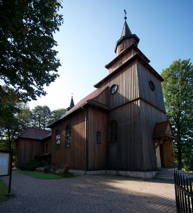 Zdjęcie nr 7: Kościół drewniany na podmurówce z kamienia, o konstrukcji zrębowej, szalowany; jednonawowy, orientowany; wieża o konstrukcji słupowej.
Prezbiterium na planie prostokąta zamkniętego trójbocznie, od północy przylega prostokątna w rzucie zakrystia; nawa na planie prostokąta, z przylegającą od południa kruchtą na rzucie kwadratu; dobudowana nawa na planie dłuższego od poprzedniej prostokąta, od zachodu wieża na planie kwadratu, częściowo wtopiona w ścianę zamykającą nawę, z wyodrębnionymi dwoma pomieszczeniami flankującymi ją.
Nawy i prezbiterium nakryte stropami, oddzielone od siebie szerokimi arkadami zamkniętymi łukami odcinkowymi. W zachodniej części większej nawy prosty parapet chóru muzycznego wsparty na dwóch drewnianych filarach; prospekt organowy przepruwa strop w przestrzeń wieży. Posadzka z płyt ceramicznych. Otwory okienne w formie stojącego prostokąta zamkniętego łukiem półkolistym, obwiedzione listwowymi opaskami, z kwaterowymi podziałami; od strony południowej – jedno w prezbiterium i po dwa w każdej części nawy, od strony północnej po dwa w każdej części nawy, od zachodniej dwa niewielkie flankujące wieżę. W zakrystii analogiczny otwór okienny od wschodu i mniejszy od północy. Otwory wejściowe: z prezbiterium do zakrystii drzwi płycinowe w futrynie; w przejściu z mniejszej nawy do kruchty drzwi płycinowe w futrynie; w przejściu z przyziemia wieży do większej nawy otwór w formie stojącego prostokąta z wklęsłymi górnymi narożami, obwiedziony listwowymi opaskami. 
Ściany z zewnątrz szalowane z listwowaniem. Trzy dachy z osobnymi kalenicami, nad prezbiterium wielospadowy; nad dwiema nawami dwuspadowe, zakończone daszkami okapowymi; kryte ceramiczną dachówką. Wieżyczka na sygnaturkę na kalenicy nad mniejszą nawą, obita blachą, zamknięta daszkiem wieżowym. 
Wieża o ścianach zwężających się ku górze, trójkondygnacyjna. Dolna kondygnacja zamknięta gzymsem, a dwie wyższe daszkami okapowymi. Całość zwieńczona hełmem ostrosłupowym z latarnią przeprutą oknami. Otwory okienne: w pierwszej kondygnacji na ścianie wschodniej i zachodniej w formie stojącego prostokąta zamkniętego łukiem półkolistym, obwiedzione listwowymi opaskami, z kwaterowymi podziałami; w drugiej kondygnacji z trzech stron okulusy, w trzeciej z czterech stron niewielkie okienka. Otwór wejściowy od zachodu, na pięciu kamiennych stopniach, drzwi deskowe-spągowe, dwuskrzydłowe, w odrzwiach belkowych; nakryty daszkiem dwuspadowym.
