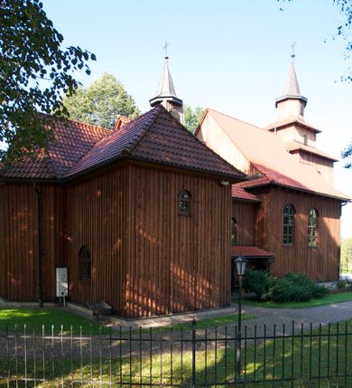 Zdjęcie nr 12: Kościół drewniany na podmurówce z kamienia, o konstrukcji zrębowej, szalowany; jednonawowy, orientowany; wieża o konstrukcji słupowej.
Prezbiterium na planie prostokąta zamkniętego trójbocznie, od północy przylega prostokątna w rzucie zakrystia; nawa na planie prostokąta, z przylegającą od południa kruchtą na rzucie kwadratu; dobudowana nawa na planie dłuższego od poprzedniej prostokąta, od zachodu wieża na planie kwadratu, częściowo wtopiona w ścianę zamykającą nawę, z wyodrębnionymi dwoma pomieszczeniami flankującymi ją.
Nawy i prezbiterium nakryte stropami, oddzielone od siebie szerokimi arkadami zamkniętymi łukami odcinkowymi. W zachodniej części większej nawy prosty parapet chóru muzycznego wsparty na dwóch drewnianych filarach; prospekt organowy przepruwa strop w przestrzeń wieży. Posadzka z płyt ceramicznych. Otwory okienne w formie stojącego prostokąta zamkniętego łukiem półkolistym, obwiedzione listwowymi opaskami, z kwaterowymi podziałami; od strony południowej – jedno w prezbiterium i po dwa w każdej części nawy, od strony północnej po dwa w każdej części nawy, od zachodniej dwa niewielkie flankujące wieżę. W zakrystii analogiczny otwór okienny od wschodu i mniejszy od północy. Otwory wejściowe: z prezbiterium do zakrystii drzwi płycinowe w futrynie; w przejściu z mniejszej nawy do kruchty drzwi płycinowe w futrynie; w przejściu z przyziemia wieży do większej nawy otwór w formie stojącego prostokąta z wklęsłymi górnymi narożami, obwiedziony listwowymi opaskami. 
Ściany z zewnątrz szalowane z listwowaniem. Trzy dachy z osobnymi kalenicami, nad prezbiterium wielospadowy; nad dwiema nawami dwuspadowe, zakończone daszkami okapowymi; kryte ceramiczną dachówką. Wieżyczka na sygnaturkę na kalenicy nad mniejszą nawą, obita blachą, zamknięta daszkiem wieżowym. 
Wieża o ścianach zwężających się ku górze, trójkondygnacyjna. Dolna kondygnacja zamknięta gzymsem, a dwie wyższe daszkami okapowymi. Całość zwieńczona hełmem ostrosłupowym z latarnią przeprutą oknami. Otwory okienne: w pierwszej kondygnacji na ścianie wschodniej i zachodniej w formie stojącego prostokąta zamkniętego łukiem półkolistym, obwiedzione listwowymi opaskami, z kwaterowymi podziałami; w drugiej kondygnacji z trzech stron okulusy, w trzeciej z czterech stron niewielkie okienka. Otwór wejściowy od zachodu, na pięciu kamiennych stopniach, drzwi deskowe-spągowe, dwuskrzydłowe, w odrzwiach belkowych; nakryty daszkiem dwuspadowym.
