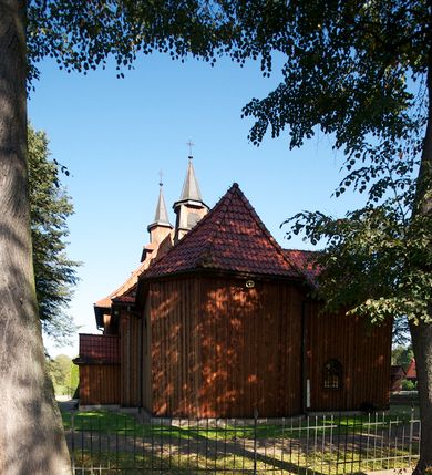 Zdjęcie nr 10: Kościół drewniany na podmurówce z kamienia, o konstrukcji zrębowej, szalowany; jednonawowy, orientowany; wieża o konstrukcji słupowej.
Prezbiterium na planie prostokąta zamkniętego trójbocznie, od północy przylega prostokątna w rzucie zakrystia; nawa na planie prostokąta, z przylegającą od południa kruchtą na rzucie kwadratu; dobudowana nawa na planie dłuższego od poprzedniej prostokąta, od zachodu wieża na planie kwadratu, częściowo wtopiona w ścianę zamykającą nawę, z wyodrębnionymi dwoma pomieszczeniami flankującymi ją.
Nawy i prezbiterium nakryte stropami, oddzielone od siebie szerokimi arkadami zamkniętymi łukami odcinkowymi. W zachodniej części większej nawy prosty parapet chóru muzycznego wsparty na dwóch drewnianych filarach; prospekt organowy przepruwa strop w przestrzeń wieży. Posadzka z płyt ceramicznych. Otwory okienne w formie stojącego prostokąta zamkniętego łukiem półkolistym, obwiedzione listwowymi opaskami, z kwaterowymi podziałami; od strony południowej – jedno w prezbiterium i po dwa w każdej części nawy, od strony północnej po dwa w każdej części nawy, od zachodniej dwa niewielkie flankujące wieżę. W zakrystii analogiczny otwór okienny od wschodu i mniejszy od północy. Otwory wejściowe: z prezbiterium do zakrystii drzwi płycinowe w futrynie; w przejściu z mniejszej nawy do kruchty drzwi płycinowe w futrynie; w przejściu z przyziemia wieży do większej nawy otwór w formie stojącego prostokąta z wklęsłymi górnymi narożami, obwiedziony listwowymi opaskami. 
Ściany z zewnątrz szalowane z listwowaniem. Trzy dachy z osobnymi kalenicami, nad prezbiterium wielospadowy; nad dwiema nawami dwuspadowe, zakończone daszkami okapowymi; kryte ceramiczną dachówką. Wieżyczka na sygnaturkę na kalenicy nad mniejszą nawą, obita blachą, zamknięta daszkiem wieżowym. 
Wieża o ścianach zwężających się ku górze, trójkondygnacyjna. Dolna kondygnacja zamknięta gzymsem, a dwie wyższe daszkami okapowymi. Całość zwieńczona hełmem ostrosłupowym z latarnią przeprutą oknami. Otwory okienne: w pierwszej kondygnacji na ścianie wschodniej i zachodniej w formie stojącego prostokąta zamkniętego łukiem półkolistym, obwiedzione listwowymi opaskami, z kwaterowymi podziałami; w drugiej kondygnacji z trzech stron okulusy, w trzeciej z czterech stron niewielkie okienka. Otwór wejściowy od zachodu, na pięciu kamiennych stopniach, drzwi deskowe-spągowe, dwuskrzydłowe, w odrzwiach belkowych; nakryty daszkiem dwuspadowym.
