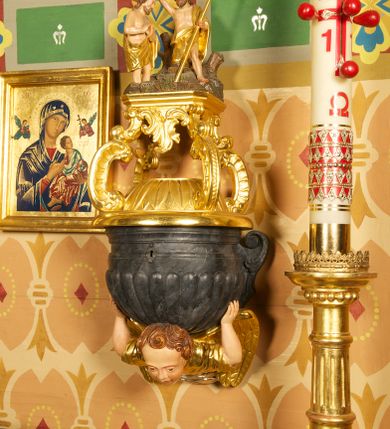 Zdjęcie nr 3: Półkolista misa o płaszczu z imitacją puklowania i brzegiem w formie profilowanego gzymsu. Ujęta uszami w kształcie wolut przytwierdzonych do ściany. Podstawę misy tworzy rzeźbiona półpostać anioła wyłaniającego się z obłoku, który dźwiga ją na plecach i ujmuje uniesionymi w górę rękami. Twarz ma pociągłą, o pełnych policzkach i wysokim czole, dużych, migdałowatych oczach, szerokim nosie i rozchylonych, wąskich ustach. Głowę okalają krótkie, silnie kręcone włosy. Anioł ubrany w złoconą tunikę z podwiniętymi rękawami. Skrzydła złocone, złożone. Pokrywa złożona z podstawy na planie ściętego koła, z wybrzuszeniem dekorowanym liśćmi, na niej cztery rocaille&#039;owe kabłąki, dźwigające prostokątną podstawę, na której umieszczona jest niewielka grupa rzeźbiarska ze sceną Chrztu Chrystusa. Misa polichromowana na sposób imitujący marmoryzację. 

