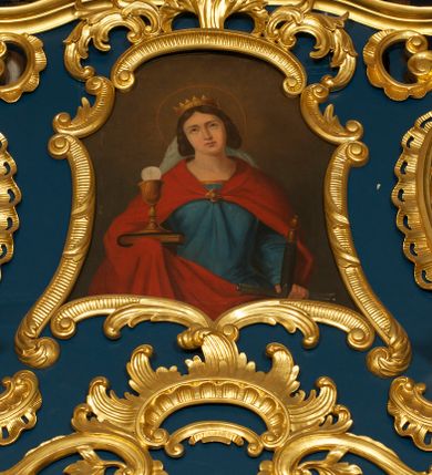 Zdjęcie nr 1: Obraz o fantazyjnej formie zbliżonej do trapezu, od góry zamknięty łukiem odcinkowym z uskokiem, o wklęsłych bokach  i dolnej krawędzi. W centrum kompozycji św. Barbara ukazana frontalnie, w półpostaci. Głowa lekko przechylona w prawo. W lewej opuszczonej ręce trzyma rękojeść miecza skierowanego w dół, w prawej podtrzymuje księgę, na której stoi kielich z hostią. Twarz ma owalną, o regularnych rysach, owalnych oczach skierowanych w górę, prostych łukach brwiowych, wąskim prostym nosie oraz małych ustach. Włosy upięte po bokach głowy. Na głowie ma koronę otwartą. Ubrana jest w niebieską suknię o złoconej lamówce oraz czerwony płaszcz zarzucony na ramiona i zapięty na piersi klamrą w formie kwiatu. Z tyłu głowy widoczny biały welon. Głowę świętej otacza nimb. Postać ukazana na cieniowanym, brązowym tle, rozjaśnionym w górnej części obrazu. 
