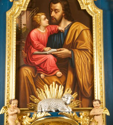 Zdjęcie nr 1: Obraz w formie stojącego prostokąta zamkniętego łukiem półkolistym. W centrum kompozycji ukazany św. Józef trzymający na kolanach Dzieciątko Jezus i nauczający je. Józef przedstawiony w pozycji siedzącej, do wysokości łydek, zwrócony w trzech czwartych w lewo. Prawą ręką obejmuje Dzieciątko, lewą przytrzymuje otwartą księgę na jego kolanach Twarz ma pociągłą, o wysokim czole, dużych, okrągłych oczach, skierowanych w dół, garbatym nosie i pełnych ustach; okoloną kręconymi włosami sięgającymi ramion oraz krótką brodą i wąsami. Nad głową Józefa nimb. Ubrany jest w niebieską tunikę ze złoconą lamówką oraz obficie drapowany żółty płaszcz przewiązany przez lewe ramię i opadający na kolana. Dzieciątko w pozycji siedzącej, zwrócone w trzech czwartych w prawo, z głową ukazaną z profilu. Lewą, ugiętą rękę opiera na piersi Józefa, prawą kładzie na księdze, opartej na jego kolanach. Nogi ma skrzyżowane. Twarz o młodzieńczych rysach, dużych oczach skierowanych w górę, małym nosie i pełnych ustach, okoloną jasnymi, kręconymi włosami. Dzieciątko ubrane w jasnoczerwoną, luźną i silnie drapowaną tunikę ze złoconą lamówką. Nad głową Dzieciątka nimb z krzyżem. Scena ukazana we wnętrzu z widocznym po lewej tronie oknem, na którego parapecie stoi wazon z gałązką lilii oraz po którym pnie się winna latorośl. 
