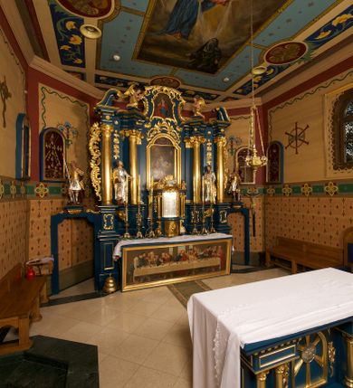 Zdjęcie nr 3: Ołtarz drewniany, prostopadłościenny, z kamienną mensą. Antepedium w formie obrazu z przedstawieniem Ostatniej Wieczerzy, ujętego profilowaną ramą. Na ołtarzu ustawione tabernakulum z tronem wystawienia. 
Nastawa architektoniczna, jednokondygnacyjna ze zwieńczeniem, trójosiowa z bramkami, ustawiona na dwustrefowym cokole z wyłamanymi czterema prostopadłościanami. Oś środkowa ujęta dwiema parami pilastrów oraz parą kolumn, na cokołach zwróconych pod kątem do wewnątrz ołtarza. Osie zewnętrzne ujęte parą pilastrów i stojących na ich tle kolumn. Wszystkie podpory dźwigają imposty, na osiach środkowy podpór zwrócone pod kątem do wewnątrz. Na parze skrajnych impostów fragmenty przerwanego, falistego przyczółka. W polu środkowym nisza w formie stojącego prostokąta zamkniętego łukiem półkolistym nadwieszonym, z uskokiem, ujęta profilowaną ramą, z obrazem Nauczania Marii. Na osiach bocznych figury św. Piotra i św. Pawła ustawione na wspornikach Zwieńczenie niearchitektoniczne, o formie zbliżonej do trapezu, o wklęsłych bokach z uszakami, zamknięte fragmentem falistego gzymsu. W polu obraz o fantazyjnej formie zbliżonej do trapezu z przedstawieniem św. Barbary, ujęty ornamentalną ramą. Zwieńczenie flankują dwie figury klęczących aniołów na cokołach. Nastawa dekorowana rocaille'm w przestrzeni nad polem głównym oraz w partii zwieńczenia, ujęta uszami utworzonymi z rocaille'u, kampanuli i ornamentu roślinnego. Na osiach bocznych zwisy kwiatowe. Bramki w formie przejść o wykroju stojącego prostokąta o wklęsłych górnych narożach, zamkniętego dwiema woltami i cokołami z imitacją puklowania, na których stoją figury niezidentyfikowanych monarchów. Struktura polichromowana w kolorze niebieskim, kolumny, profile i ornamentyka złocone. 






