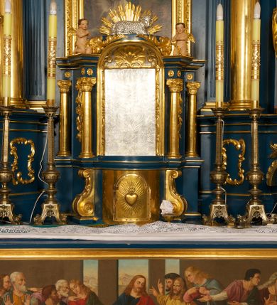 Zdjęcie nr 4: Ołtarz drewniany, prostopadłościenny, z kamienną mensą. Antepedium w formie obrazu z przedstawieniem Ostatniej Wieczerzy, ujętego profilowaną ramą. Na ołtarzu ustawione tabernakulum z tronem wystawienia. 
Nastawa architektoniczna, jednokondygnacyjna ze zwieńczeniem, trójosiowa z bramkami, ustawiona na dwustrefowym cokole z wyłamanymi czterema prostopadłościanami. Oś środkowa ujęta dwiema parami pilastrów oraz parą kolumn, na cokołach zwróconych pod kątem do wewnątrz ołtarza. Osie zewnętrzne ujęte parą pilastrów i stojących na ich tle kolumn. Wszystkie podpory dźwigają imposty, na osiach środkowy podpór zwrócone pod kątem do wewnątrz. Na parze skrajnych impostów fragmenty przerwanego, falistego przyczółka. W polu środkowym nisza w formie stojącego prostokąta zamkniętego łukiem półkolistym nadwieszonym, z uskokiem, ujęta profilowaną ramą, z obrazem Nauczania Marii. Na osiach bocznych figury św. Piotra i św. Pawła ustawione na wspornikach Zwieńczenie niearchitektoniczne, o formie zbliżonej do trapezu, o wklęsłych bokach z uszakami, zamknięte fragmentem falistego gzymsu. W polu obraz o fantazyjnej formie zbliżonej do trapezu z przedstawieniem św. Barbary, ujęty ornamentalną ramą. Zwieńczenie flankują dwie figury klęczących aniołów na cokołach. Nastawa dekorowana rocaille'm w przestrzeni nad polem głównym oraz w partii zwieńczenia, ujęta uszami utworzonymi z rocaille'u, kampanuli i ornamentu roślinnego. Na osiach bocznych zwisy kwiatowe. Bramki w formie przejść o wykroju stojącego prostokąta o wklęsłych górnych narożach, zamkniętego dwiema woltami i cokołami z imitacją puklowania, na których stoją figury niezidentyfikowanych monarchów. Struktura polichromowana w kolorze niebieskim, kolumny, profile i ornamentyka złocone. 






