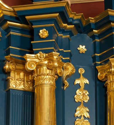 Zdjęcie nr 15: Ołtarz drewniany, prostopadłościenny, z kamienną mensą. Antepedium w formie obrazu z przedstawieniem Ostatniej Wieczerzy, ujętego profilowaną ramą. Na ołtarzu ustawione tabernakulum z tronem wystawienia. 
Nastawa architektoniczna, jednokondygnacyjna ze zwieńczeniem, trójosiowa z bramkami, ustawiona na dwustrefowym cokole z wyłamanymi czterema prostopadłościanami. Oś środkowa ujęta dwiema parami pilastrów oraz parą kolumn, na cokołach zwróconych pod kątem do wewnątrz ołtarza. Osie zewnętrzne ujęte parą pilastrów i stojących na ich tle kolumn. Wszystkie podpory dźwigają imposty, na osiach środkowy podpór zwrócone pod kątem do wewnątrz. Na parze skrajnych impostów fragmenty przerwanego, falistego przyczółka. W polu środkowym nisza w formie stojącego prostokąta zamkniętego łukiem półkolistym nadwieszonym, z uskokiem, ujęta profilowaną ramą, z obrazem Nauczania Marii. Na osiach bocznych figury św. Piotra i św. Pawła ustawione na wspornikach Zwieńczenie niearchitektoniczne, o formie zbliżonej do trapezu, o wklęsłych bokach z uszakami, zamknięte fragmentem falistego gzymsu. W polu obraz o fantazyjnej formie zbliżonej do trapezu z przedstawieniem św. Barbary, ujęty ornamentalną ramą. Zwieńczenie flankują dwie figury klęczących aniołów na cokołach. Nastawa dekorowana rocaille'm w przestrzeni nad polem głównym oraz w partii zwieńczenia, ujęta uszami utworzonymi z rocaille'u, kampanuli i ornamentu roślinnego. Na osiach bocznych zwisy kwiatowe. Bramki w formie przejść o wykroju stojącego prostokąta o wklęsłych górnych narożach, zamkniętego dwiema woltami i cokołami z imitacją puklowania, na których stoją figury niezidentyfikowanych monarchów. Struktura polichromowana w kolorze niebieskim, kolumny, profile i ornamentyka złocone. 






