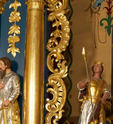 Zdjęcie nr 16: Ołtarz drewniany, prostopadłościenny, z kamienną mensą. Antepedium w formie obrazu z przedstawieniem Ostatniej Wieczerzy, ujętego profilowaną ramą. Na ołtarzu ustawione tabernakulum z tronem wystawienia. 
Nastawa architektoniczna, jednokondygnacyjna ze zwieńczeniem, trójosiowa z bramkami, ustawiona na dwustrefowym cokole z wyłamanymi czterema prostopadłościanami. Oś środkowa ujęta dwiema parami pilastrów oraz parą kolumn, na cokołach zwróconych pod kątem do wewnątrz ołtarza. Osie zewnętrzne ujęte parą pilastrów i stojących na ich tle kolumn. Wszystkie podpory dźwigają imposty, na osiach środkowy podpór zwrócone pod kątem do wewnątrz. Na parze skrajnych impostów fragmenty przerwanego, falistego przyczółka. W polu środkowym nisza w formie stojącego prostokąta zamkniętego łukiem półkolistym nadwieszonym, z uskokiem, ujęta profilowaną ramą, z obrazem Nauczania Marii. Na osiach bocznych figury św. Piotra i św. Pawła ustawione na wspornikach Zwieńczenie niearchitektoniczne, o formie zbliżonej do trapezu, o wklęsłych bokach z uszakami, zamknięte fragmentem falistego gzymsu. W polu obraz o fantazyjnej formie zbliżonej do trapezu z przedstawieniem św. Barbary, ujęty ornamentalną ramą. Zwieńczenie flankują dwie figury klęczących aniołów na cokołach. Nastawa dekorowana rocaille'm w przestrzeni nad polem głównym oraz w partii zwieńczenia, ujęta uszami utworzonymi z rocaille'u, kampanuli i ornamentu roślinnego. Na osiach bocznych zwisy kwiatowe. Bramki w formie przejść o wykroju stojącego prostokąta o wklęsłych górnych narożach, zamkniętego dwiema woltami i cokołami z imitacją puklowania, na których stoją figury niezidentyfikowanych monarchów. Struktura polichromowana w kolorze niebieskim, kolumny, profile i ornamentyka złocone. 







