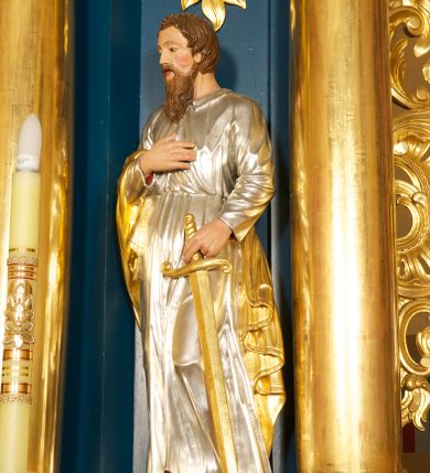 Zdjęcie nr 1: Rzeźba pełnoplastyczna, ustawiona na niskiej podstawie. Figura ukazana frontalnie, w kontrapoście, z głową skierowaną w prawo. W lewej, opuszczonej ręce trzyma przy boku miecz, skierowany ostrzem w dół, prawą kładzie na piersi. Twarz ma szeroką, o niskim czole, niewielkich, migdałowatych i półprzymkniętych oczach, małym nosie i rozchylonych ustach. Włosy lekko falowane, krótkie, silnie przylegające do głowy. Twarz okolona długą lekko falowaną brodą i wąsami. Postać ubrana w długą, srebrzoną tunikę z kołnierzykiem, przepasaną w pasie oraz złocony płaszcz przerzucony przez prawe ramię i opadający na plecy i lewy bok. Na stopach ma złocone sandały. Polichromia ciała naturalistyczna. 






