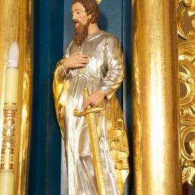 Zdjęcie nr 1: Rzeźba pełnoplastyczna, ustawiona na niskiej podstawie. Figura ukazana frontalnie, w kontrapoście, z głową skierowaną w prawo. W lewej, opuszczonej ręce trzyma przy boku miecz, skierowany ostrzem w dół, prawą kładzie na piersi. Twarz ma szeroką, o niskim czole, niewielkich, migdałowatych i półprzymkniętych oczach, małym nosie i rozchylonych ustach. Włosy lekko falowane, krótkie, silnie przylegające do głowy. Twarz okolona długą lekko falowaną brodą i wąsami. Postać ubrana w długą, srebrzoną tunikę z kołnierzykiem, przepasaną w pasie oraz złocony płaszcz przerzucony przez prawe ramię i opadający na plecy i lewy bok. Na stopach ma złocone sandały. Polichromia ciała naturalistyczna. 






