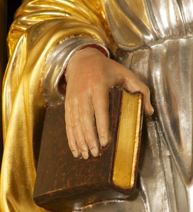 Zdjęcie nr 4: Rzeźba pełnoplastyczna, ustawiona na niskiej podstawie. Figura ukazana frontalnie, w lekkim odchyleniu, z uniesioną głową skierowaną w lewo. W lewej, wyciągniętej do przodu ręce trzyma skrzyżowane dwa klucze, w prawej, ugiętej ręce trzyma zamkniętą księgę, opartą na ugiętej nodze, ustawionej na stopniu. Twarz ma szeroką, o wysokim czole, niewielkich migdałowatych oczach, małych nosie i ustach. Włosy lekko kręcone, krótkie, silnie przylegające do głowy, z zaznaczoną łysiną i puklem nad czołem. Twarz okolona krótką, kręconą brodą z wąsami. Postać ubrana w długą, srebrzoną tunikę z kołnierzykiem, przepasaną w pasie oraz złocony płaszcz przerzucony przez prawe ramię i opadający na plecy. Na stopach ma złocone sandały. Polichromią ciała naturalistyczna. 






