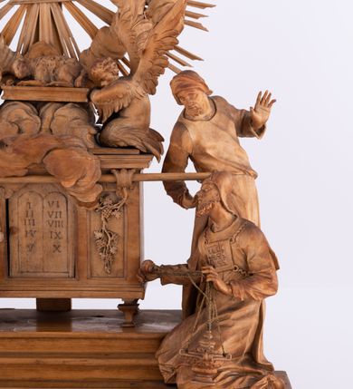 Zdjęcie nr 3: Tabernakulum w formie Arki Przymierza, adorowanej przez dwie klęczące figury św. Jana i starotestamentowego arcykapłana, dwie stojące postacie lewitów oraz klęczących aniołów, zwieńczonej glorią promienistą z okiem Opatrzności. Arka w formie prostopadłościennej szafki z dwoma drążkami do noszenia jest od frontu podzielone na trzy pola: środkowe zamknięte łukiem wklęsło-wypukłym i boczne o ćwierćkoliście wyciętych narożach. Pole środkowe stanowią drzwiczki z rytymi cyframi Dekalogu, a w bocznych znajdują się kłosy zbóż i winne grono. Na skłębionych chmurach z podestem leży baranek. Nad nim widnieje znacznej wielkości gloria promienista z wieńcem chmur i umieszczonym w nim okiem Opatrzności oraz cztery uskrzydlone główki anielskie. Nad parą główek w górnej części papieska tiara ze skrzyżowanymi kluczami. Po bokach baranka dwa klęczące, uskrzydlone nagie aniołki o rękach i nogach utworzonych z piór. Obok arki dwie postacie lewitów ubranych w długie szaty, w różnicowanych pozach i gestach. Poniżej klęczą postacie św. Jana z księgą i orłem obok niego i kapłana w tradycyjnym starotestamentowym stroju – efodzie czyli tunice i płaszczu wierzchnim przepasanym na biodrach, z pektorałem na piersi i czapką na głowie. 