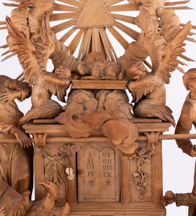 Zdjęcie nr 7: Tabernakulum w formie Arki Przymierza, adorowanej przez dwie klęczące figury św. Jana i starotestamentowego arcykapłana, dwie stojące postacie lewitów oraz klęczących aniołów, zwieńczonej glorią promienistą z okiem Opatrzności. Arka w formie prostopadłościennej szafki z dwoma drążkami do noszenia jest od frontu podzielone na trzy pola: środkowe zamknięte łukiem wklęsło-wypukłym i boczne o ćwierćkoliście wyciętych narożach. Pole środkowe stanowią drzwiczki z rytymi cyframi Dekalogu, a w bocznych znajdują się kłosy zbóż i winne grono. Na skłębionych chmurach z podestem leży baranek. Nad nim widnieje znacznej wielkości gloria promienista z wieńcem chmur i umieszczonym w nim okiem Opatrzności oraz cztery uskrzydlone główki anielskie. Nad parą główek w górnej części papieska tiara ze skrzyżowanymi kluczami. Po bokach baranka dwa klęczące, uskrzydlone nagie aniołki o rękach i nogach utworzonych z piór. Obok arki dwie postacie lewitów ubranych w długie szaty, w różnicowanych pozach i gestach. Poniżej klęczą postacie św. Jana z księgą i orłem obok niego i kapłana w tradycyjnym starotestamentowym stroju – efodzie czyli tunice i płaszczu wierzchnim przepasanym na biodrach, z pektorałem na piersi i czapką na głowie. 