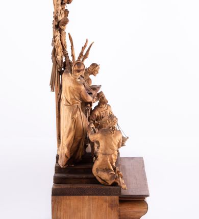 Zdjęcie nr 13: Tabernakulum w formie Arki Przymierza, adorowanej przez dwie klęczące figury św. Jana i starotestamentowego arcykapłana, dwie stojące postacie lewitów oraz klęczących aniołów, zwieńczonej glorią promienistą z okiem Opatrzności. Arka w formie prostopadłościennej szafki z dwoma drążkami do noszenia jest od frontu podzielone na trzy pola: środkowe zamknięte łukiem wklęsło-wypukłym i boczne o ćwierćkoliście wyciętych narożach. Pole środkowe stanowią drzwiczki z rytymi cyframi Dekalogu, a w bocznych znajdują się kłosy zbóż i winne grono. Na skłębionych chmurach z podestem leży baranek. Nad nim widnieje znacznej wielkości gloria promienista z wieńcem chmur i umieszczonym w nim okiem Opatrzności oraz cztery uskrzydlone główki anielskie. Nad parą główek w górnej części papieska tiara ze skrzyżowanymi kluczami. Po bokach baranka dwa klęczące, uskrzydlone nagie aniołki o rękach i nogach utworzonych z piór. Obok arki dwie postacie lewitów ubranych w długie szaty, w różnicowanych pozach i gestach. Poniżej klęczą postacie św. Jana z księgą i orłem obok niego i kapłana w tradycyjnym starotestamentowym stroju – efodzie czyli tunice i płaszczu wierzchnim przepasanym na biodrach, z pektorałem na piersi i czapką na głowie. 