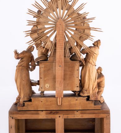 Zdjęcie nr 12: Tabernakulum w formie Arki Przymierza, adorowanej przez dwie klęczące figury św. Jana i starotestamentowego arcykapłana, dwie stojące postacie lewitów oraz klęczących aniołów, zwieńczonej glorią promienistą z okiem Opatrzności. Arka w formie prostopadłościennej szafki z dwoma drążkami do noszenia jest od frontu podzielone na trzy pola: środkowe zamknięte łukiem wklęsło-wypukłym i boczne o ćwierćkoliście wyciętych narożach. Pole środkowe stanowią drzwiczki z rytymi cyframi Dekalogu, a w bocznych znajdują się kłosy zbóż i winne grono. Na skłębionych chmurach z podestem leży baranek. Nad nim widnieje znacznej wielkości gloria promienista z wieńcem chmur i umieszczonym w nim okiem Opatrzności oraz cztery uskrzydlone główki anielskie. Nad parą główek w górnej części papieska tiara ze skrzyżowanymi kluczami. Po bokach baranka dwa klęczące, uskrzydlone nagie aniołki o rękach i nogach utworzonych z piór. Obok arki dwie postacie lewitów ubranych w długie szaty, w różnicowanych pozach i gestach. Poniżej klęczą postacie św. Jana z księgą i orłem obok niego i kapłana w tradycyjnym starotestamentowym stroju – efodzie czyli tunice i płaszczu wierzchnim przepasanym na biodrach, z pektorałem na piersi i czapką na głowie. 