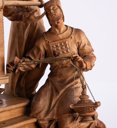 Zdjęcie nr 16: Tabernakulum w formie Arki Przymierza, adorowanej przez dwie klęczące figury św. Jana i starotestamentowego arcykapłana, dwie stojące postacie lewitów oraz klęczących aniołów, zwieńczonej glorią promienistą z okiem Opatrzności. Arka w formie prostopadłościennej szafki z dwoma drążkami do noszenia jest od frontu podzielone na trzy pola: środkowe zamknięte łukiem wklęsło-wypukłym i boczne o ćwierćkoliście wyciętych narożach. Pole środkowe stanowią drzwiczki z rytymi cyframi Dekalogu, a w bocznych znajdują się kłosy zbóż i winne grono. Na skłębionych chmurach z podestem leży baranek. Nad nim widnieje znacznej wielkości gloria promienista z wieńcem chmur i umieszczonym w nim okiem Opatrzności oraz cztery uskrzydlone główki anielskie. Nad parą główek w górnej części papieska tiara ze skrzyżowanymi kluczami. Po bokach baranka dwa klęczące, uskrzydlone nagie aniołki o rękach i nogach utworzonych z piór. Obok arki dwie postacie lewitów ubranych w długie szaty, w różnicowanych pozach i gestach. Poniżej klęczą postacie św. Jana z księgą i orłem obok niego i kapłana w tradycyjnym starotestamentowym stroju – efodzie czyli tunice i płaszczu wierzchnim przepasanym na biodrach, z pektorałem na piersi i czapką na głowie. 