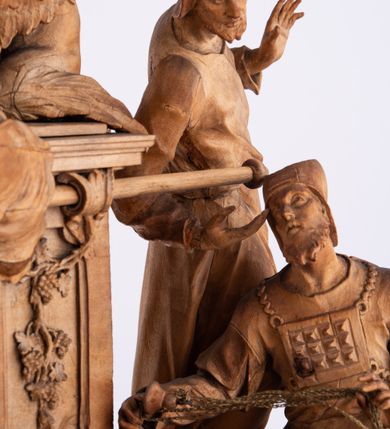 Zdjęcie nr 14: Tabernakulum w formie Arki Przymierza, adorowanej przez dwie klęczące figury św. Jana i starotestamentowego arcykapłana, dwie stojące postacie lewitów oraz klęczących aniołów, zwieńczonej glorią promienistą z okiem Opatrzności. Arka w formie prostopadłościennej szafki z dwoma drążkami do noszenia jest od frontu podzielone na trzy pola: środkowe zamknięte łukiem wklęsło-wypukłym i boczne o ćwierćkoliście wyciętych narożach. Pole środkowe stanowią drzwiczki z rytymi cyframi Dekalogu, a w bocznych znajdują się kłosy zbóż i winne grono. Na skłębionych chmurach z podestem leży baranek. Nad nim widnieje znacznej wielkości gloria promienista z wieńcem chmur i umieszczonym w nim okiem Opatrzności oraz cztery uskrzydlone główki anielskie. Nad parą główek w górnej części papieska tiara ze skrzyżowanymi kluczami. Po bokach baranka dwa klęczące, uskrzydlone nagie aniołki o rękach i nogach utworzonych z piór. Obok arki dwie postacie lewitów ubranych w długie szaty, w różnicowanych pozach i gestach. Poniżej klęczą postacie św. Jana z księgą i orłem obok niego i kapłana w tradycyjnym starotestamentowym stroju – efodzie czyli tunice i płaszczu wierzchnim przepasanym na biodrach, z pektorałem na piersi i czapką na głowie. 