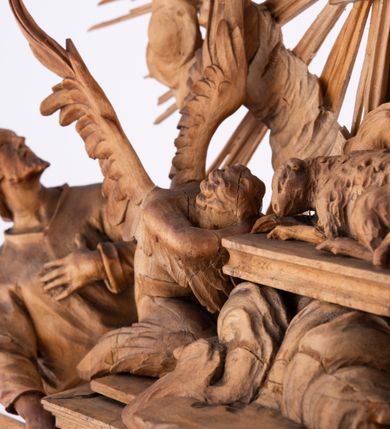 Zdjęcie nr 17: Tabernakulum w formie Arki Przymierza, adorowanej przez dwie klęczące figury św. Jana i starotestamentowego arcykapłana, dwie stojące postacie lewitów oraz klęczących aniołów, zwieńczonej glorią promienistą z okiem Opatrzności. Arka w formie prostopadłościennej szafki z dwoma drążkami do noszenia jest od frontu podzielone na trzy pola: środkowe zamknięte łukiem wklęsło-wypukłym i boczne o ćwierćkoliście wyciętych narożach. Pole środkowe stanowią drzwiczki z rytymi cyframi Dekalogu, a w bocznych znajdują się kłosy zbóż i winne grono. Na skłębionych chmurach z podestem leży baranek. Nad nim widnieje znacznej wielkości gloria promienista z wieńcem chmur i umieszczonym w nim okiem Opatrzności oraz cztery uskrzydlone główki anielskie. Nad parą główek w górnej części papieska tiara ze skrzyżowanymi kluczami. Po bokach baranka dwa klęczące, uskrzydlone nagie aniołki o rękach i nogach utworzonych z piór. Obok arki dwie postacie lewitów ubranych w długie szaty, w różnicowanych pozach i gestach. Poniżej klęczą postacie św. Jana z księgą i orłem obok niego i kapłana w tradycyjnym starotestamentowym stroju – efodzie czyli tunice i płaszczu wierzchnim przepasanym na biodrach, z pektorałem na piersi i czapką na głowie. 