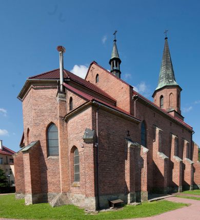 Zdjęcie nr 4: Kościół ceglany z kamiennym przyziemiem, na planie prostokąta z węższym i niższym prezbiterium flankowanym dwoma aneksami wystającymi poza lico nawy i wieżą od zachodu. Kościół orientowany, jednonawowy, czteroprzęsłowy z węższym, jednoprzęsłowym prezbiterium zamkniętym trójbocznie, z kruchtą w przyziemiu wieży. Nawa artykułowana półfilarami o ściętych narożach, przechodzących w gurty krzyżowo-żebrowego sklepienia. W nawie i prezbiterium okna prostokątne zamknięte łukiem ostrym; główne wejście od wschodu. Identyczne okna w aneksach przy prezbiterium. Aneksy dwuprzęsłowe ujęte wielobocznymi filarami, zamknięte trójbocznie z parasolowym sklepieniem. Chór muzyczny w czwartym przęśle nawy, wsparty na wielobocznych filarach z drewnianym parapetem ozdobionym ostrołukowymi blendami. Kruchta węższa od nawy, zasklepiona krzyżowo. Fasada węższa od nawy, ujęta przyporami w narożach, między którymi ostrołukowe wejście. W drugiej kondygnacji oddzielonej parapetem wysokie okno zamknięte łukiem ostrym, nad którym tarcza zegara. Nad fasadą ośmioboczna wieża. W wieży na przemian okna i płyciny, zamknięte łukiem ostrym. Trójboczne prezbiterium w narożach ujęte przyporami sięgającymi połowy wysokości, między którymi ostrołukowe okna. Aneksy na planie prostokąta z przyporami na narożach oraz jedną w części bocznej. Czteroosiowa ściana nawy i naroża oddzielone przyporami, między którymi ostrołukowo zakończone okna. Hełm wieży w formie ośmiobocznego stożka, załamującego się w partii dolnej. Nawa z dwuspadowym dachem z wieżyczką na sygnaturkę nad pierwszym przęsłem.