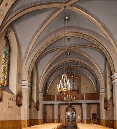 Zdjęcie nr 10: Kościół ceglany z kamiennym przyziemiem, na planie prostokąta z węższym i niższym prezbiterium flankowanym dwoma aneksami wystającymi poza lico nawy i wieżą od zachodu. Kościół orientowany, jednonawowy, czteroprzęsłowy z węższym, jednoprzęsłowym prezbiterium zamkniętym trójbocznie, z kruchtą w przyziemiu wieży. Nawa artykułowana półfilarami o ściętych narożach, przechodzących w gurty krzyżowo-żebrowego sklepienia. W nawie i prezbiterium okna prostokątne zamknięte łukiem ostrym; główne wejście od wschodu. Identyczne okna w aneksach przy prezbiterium. Aneksy dwuprzęsłowe ujęte wielobocznymi filarami, zamknięte trójbocznie z parasolowym sklepieniem. Chór muzyczny w czwartym przęśle nawy, wsparty na wielobocznych filarach z drewnianym parapetem ozdobionym ostrołukowymi blendami. Kruchta węższa od nawy, zasklepiona krzyżowo. Fasada węższa od nawy, ujęta przyporami w narożach, między którymi ostrołukowe wejście. W drugiej kondygnacji oddzielonej parapetem wysokie okno zamknięte łukiem ostrym, nad którym tarcza zegara. Nad fasadą ośmioboczna wieża. W wieży na przemian okna i płyciny, zamknięte łukiem ostrym. Trójboczne prezbiterium w narożach ujęte przyporami sięgającymi połowy wysokości, między którymi ostrołukowe okna. Aneksy na planie prostokąta z przyporami na narożach oraz jedną w części bocznej. Czteroosiowa ściana nawy i naroża oddzielone przyporami, między którymi ostrołukowo zakończone okna. Hełm wieży w formie ośmiobocznego stożka, załamującego się w partii dolnej. Nawa z dwuspadowym dachem z wieżyczką na sygnaturkę nad pierwszym przęsłem.