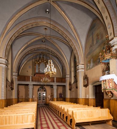 Zdjęcie nr 11: Kościół ceglany z kamiennym przyziemiem, na planie prostokąta z węższym i niższym prezbiterium flankowanym dwoma aneksami wystającymi poza lico nawy i wieżą od zachodu. Kościół orientowany, jednonawowy, czteroprzęsłowy z węższym, jednoprzęsłowym prezbiterium zamkniętym trójbocznie, z kruchtą w przyziemiu wieży. Nawa artykułowana półfilarami o ściętych narożach, przechodzących w gurty krzyżowo-żebrowego sklepienia. W nawie i prezbiterium okna prostokątne zamknięte łukiem ostrym; główne wejście od wschodu. Identyczne okna w aneksach przy prezbiterium. Aneksy dwuprzęsłowe ujęte wielobocznymi filarami, zamknięte trójbocznie z parasolowym sklepieniem. Chór muzyczny w czwartym przęśle nawy, wsparty na wielobocznych filarach z drewnianym parapetem ozdobionym ostrołukowymi blendami. Kruchta węższa od nawy, zasklepiona krzyżowo. Fasada węższa od nawy, ujęta przyporami w narożach, między którymi ostrołukowe wejście. W drugiej kondygnacji oddzielonej parapetem wysokie okno zamknięte łukiem ostrym, nad którym tarcza zegara. Nad fasadą ośmioboczna wieża. W wieży na przemian okna i płyciny, zamknięte łukiem ostrym. Trójboczne prezbiterium w narożach ujęte przyporami sięgającymi połowy wysokości, między którymi ostrołukowe okna. Aneksy na planie prostokąta z przyporami na narożach oraz jedną w części bocznej. Czteroosiowa ściana nawy i naroża oddzielone przyporami, między którymi ostrołukowo zakończone okna. Hełm wieży w formie ośmiobocznego stożka, załamującego się w partii dolnej. Nawa z dwuspadowym dachem z wieżyczką na sygnaturkę nad pierwszym przęsłem.