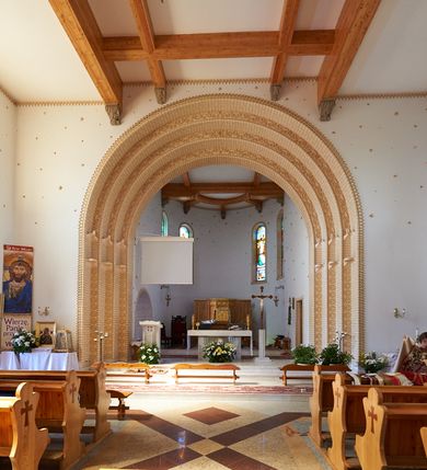 Zdjęcie nr 10: Kościół orientowany, trójnawowy, z niższym i węższym prezbiterium zakończonym absydą. Przy prezbiterium od strony południowej dostawiona kaplica na rzucie prostokąta, od północny analogiczna zakrystia, oba pomieszczenia nakryte dachami czterospadowymi. Do nawy od południa, na wysokości drugiego przęsła dostawiona zadaszona kruchta  wsparta na dwóch kamiennych filarach. Do elewacji zachodniej od południa i północy dostawione dwa aneksy na rzucie prostokąta nakryte dachami czterospadowymi. Nawa główna trójprzęsłowa, znacznie wyższa i szersza od naw bocznych, kryta stropem wspartym na murowanych z cegieł filarach o kompozytowych kapitelach. Doświetlona prostokątnymi oknami zamkniętymi łukiem półkolistym o podziale naśladującym triforium. Nawy boczne wydzielone od głównej półkolistymi arkadami, doświetlone okami w kształcie stojącego prostokąta zamkniętego półkoliście. Prezbiterium kryte prostym stropem oddzielone od nawy ścianą tęczową z półkolistą arkadą z profilowaną archiwoltą. Doświetlone wąskimi oknami w kształcie stojącego prostokąta zamkniętego łukiem półkolistym. Analogiczne okna w kaplicy południowej. W fasadzie czworoboczna zwężająca się ku górze wieża z drewnianą hurdycją, nakryta ostrosłupowym dachem zwieńczonym krzyżem. W przyziemiu portal nakryty wspartym na dwóch kamiennych filarach dachem półszczytowym. Powyżej prosty, drewniany krzyż oraz okrągła płycina mieszcząca tarczę zegarową. Elewacje licowane kamieniem, od południa i północy murowane z czerwonej cegły z kamiennymi obramieniami wokół okien. Dachy kryte blachą, ponad prezbiterium czworoboczna wieżyczka na sygnaturkę zwieńczona ostrosłupowym hełmem.